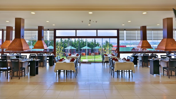 A spacious dining area with multiple tables and chairs, large windows with a view of greenery, and decorative hanging lamps. - Bon Hotel City & Resort (Silivri)