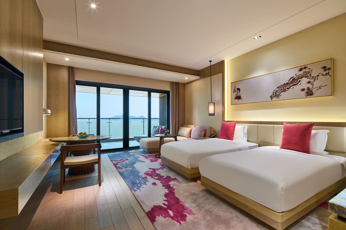 Une chambre d’hôtel avec deux lits, un coin repas, une télévision et une grande fenêtre donnant sur un beau paysage.
