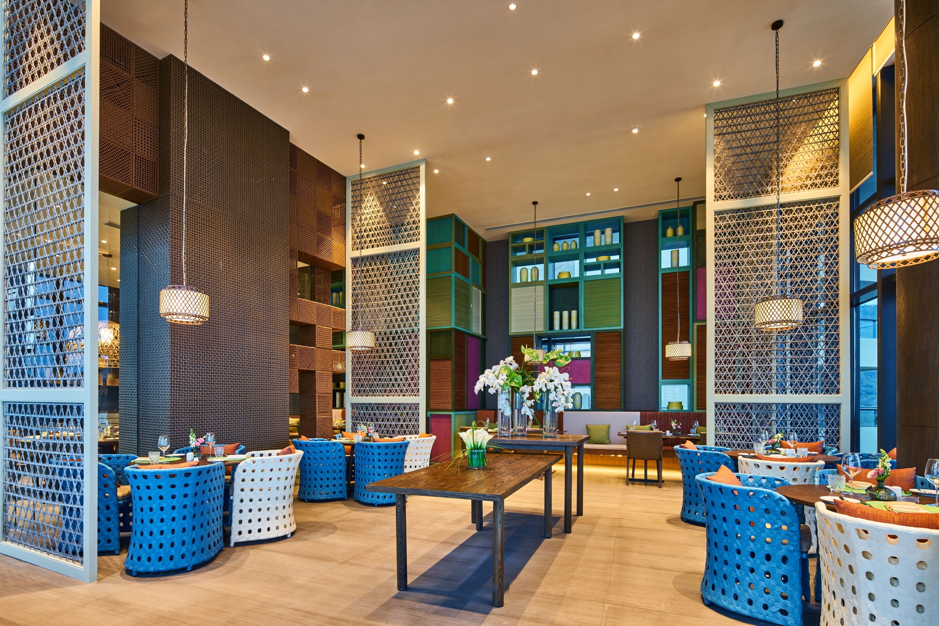 A modern hotel lobby with a central seating area, decorative lighting, and a mix of wooden and colorful furnishings.