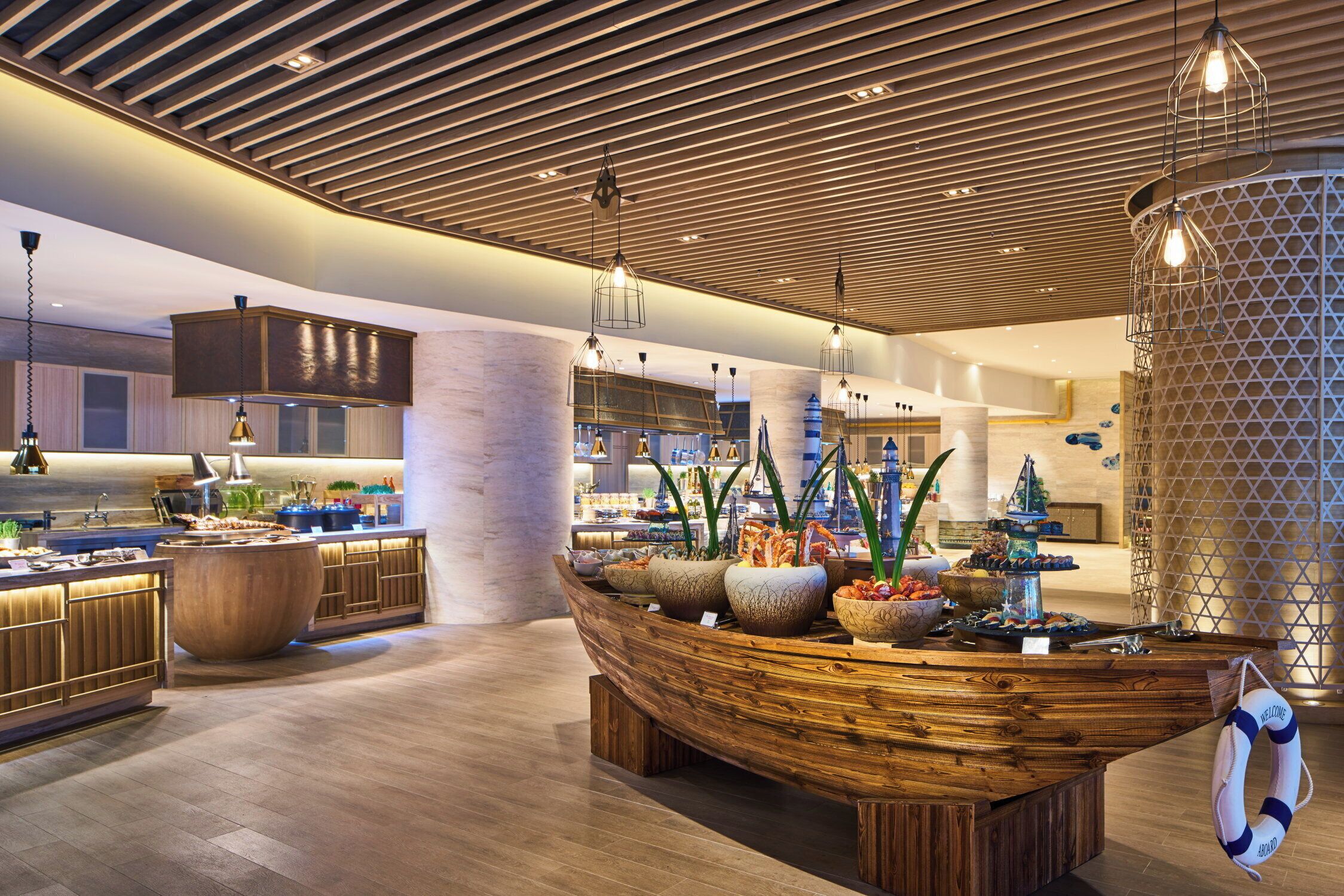 A modern kitchen with wooden cabinetry, a central island with a boat-shaped top, and a variety of food items displayed.