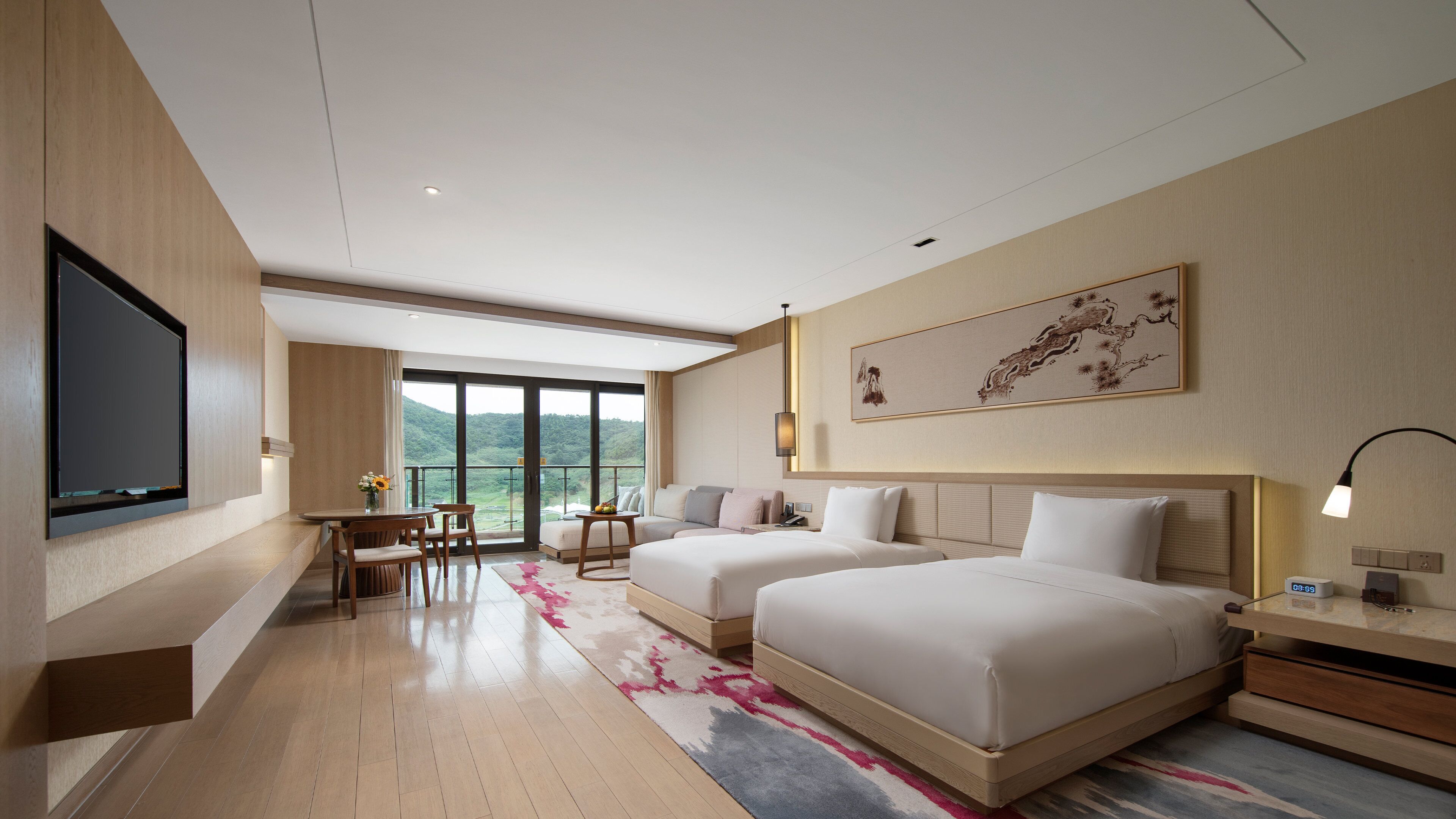 Une chambre d’hôtel dotée d’une grande télévision à écran plat, de deux lits, d’un bureau avec des chaises, d’un balcon offrant une vue sur les montagnes et d’un tableau accroché au mur.