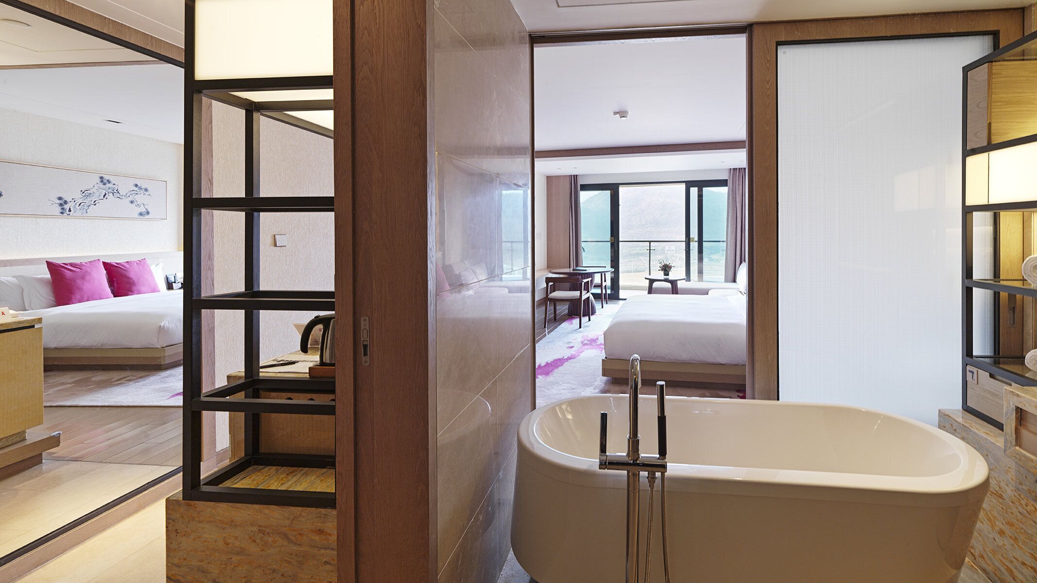 Une chambre d’hôtel moderne dotée d’une grande baignoire, d’une chambre séparée avec un lit et une vue sur la mer, ainsi que d’un balcon avec une table et des chaises.