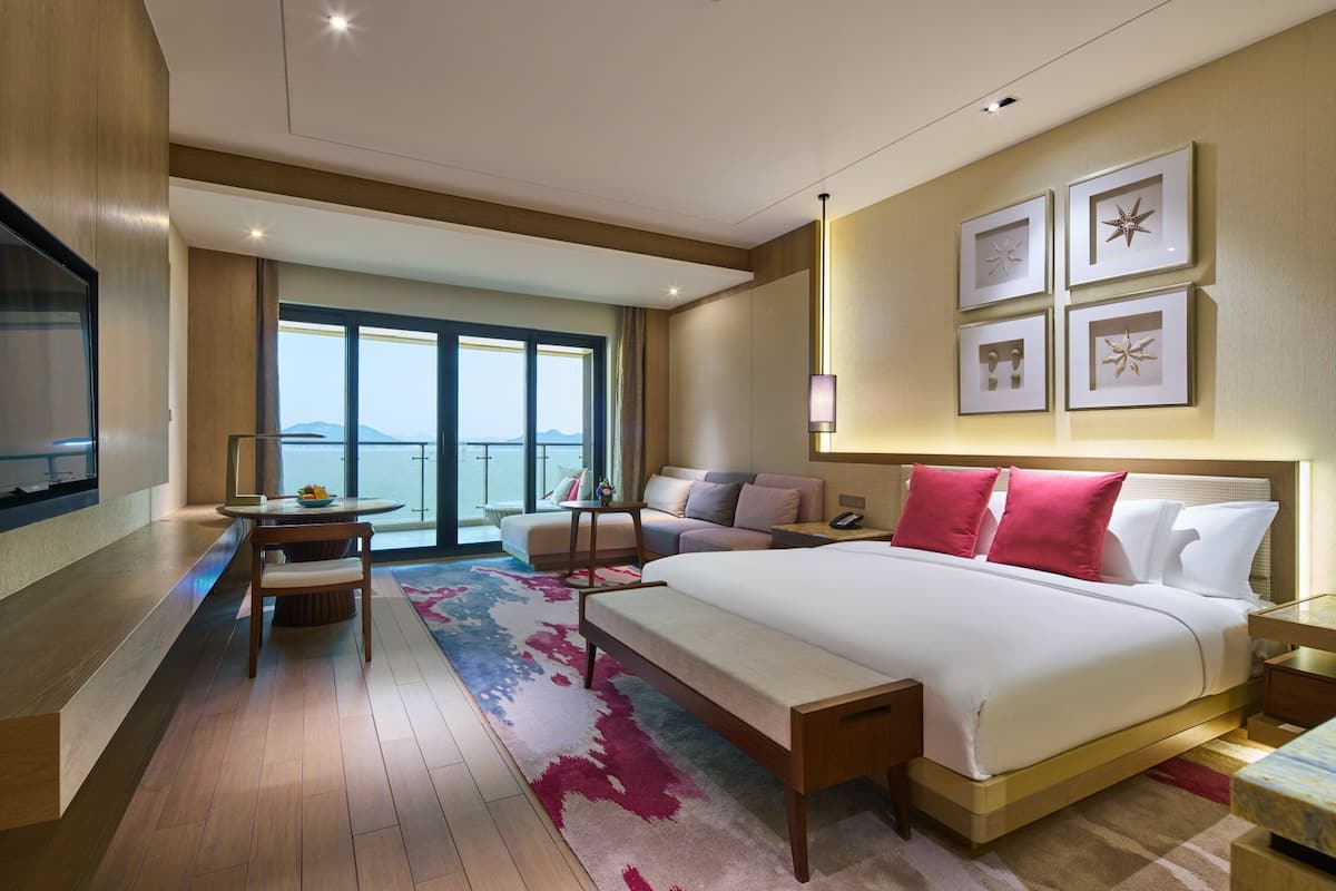 Une chambre d’hôtel moderne dotée d’un grand lit, d’un coin salon avec une table, d’une télévision et d’un balcon offrant une vue agréable.