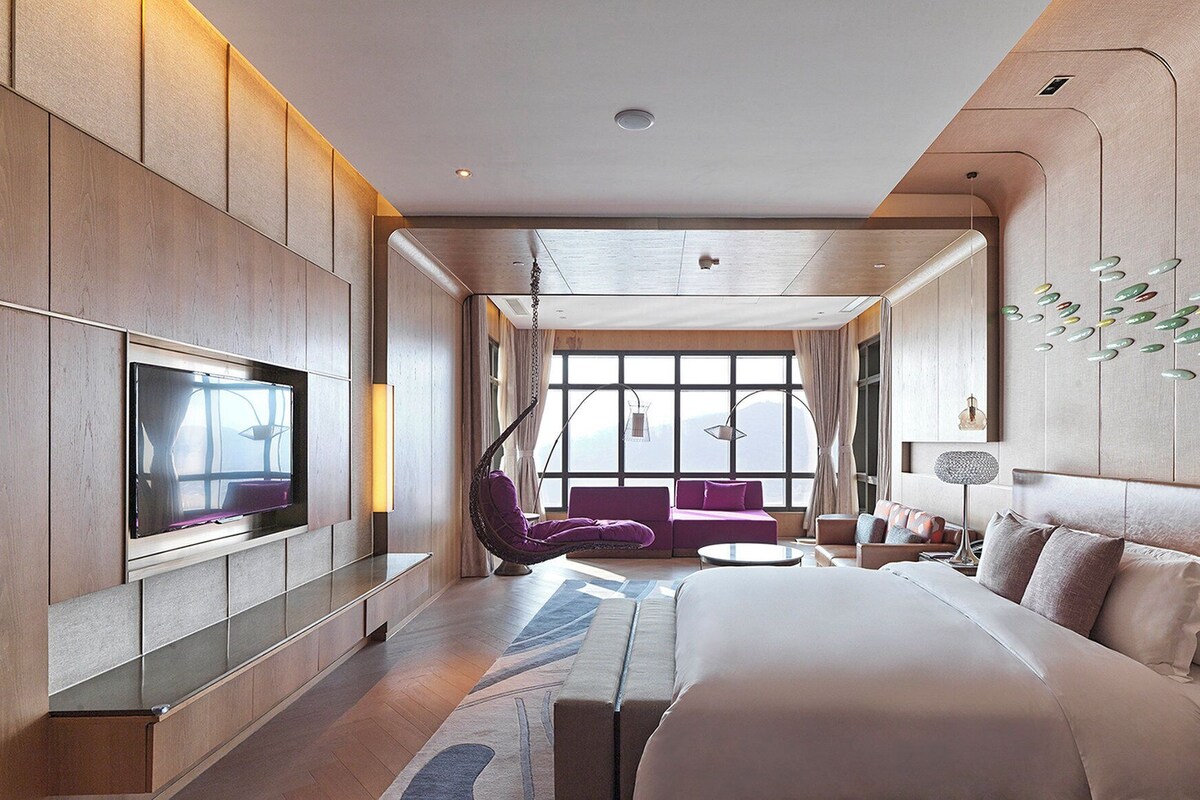 Une chambre d’hôtel moderne dotée d’un grand lit, d’une télévision à écran plat, d’un canapé et d’une table à manger.