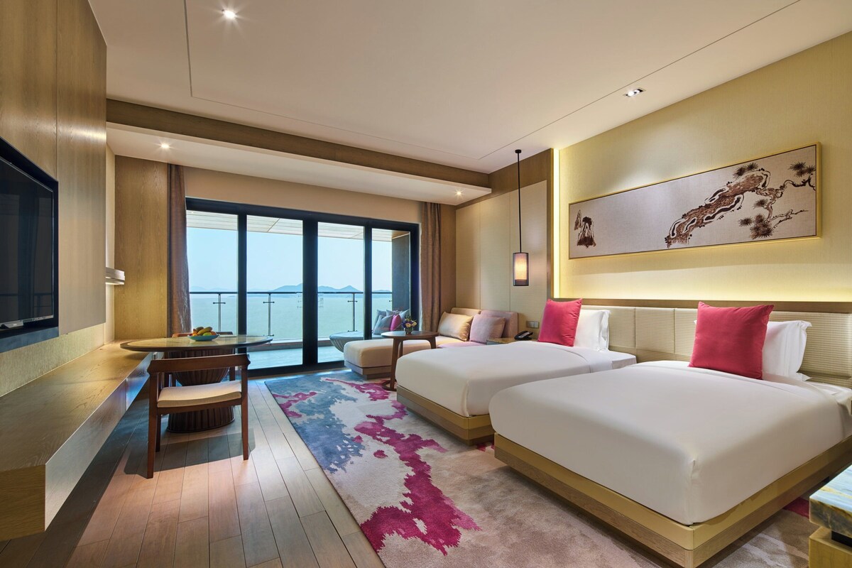 Une chambre d’hôtel avec deux lits, un coin repas comprenant une table et des chaises, une grande fenêtre offrant une vue agréable et une œuvre d’art accrochée au mur.