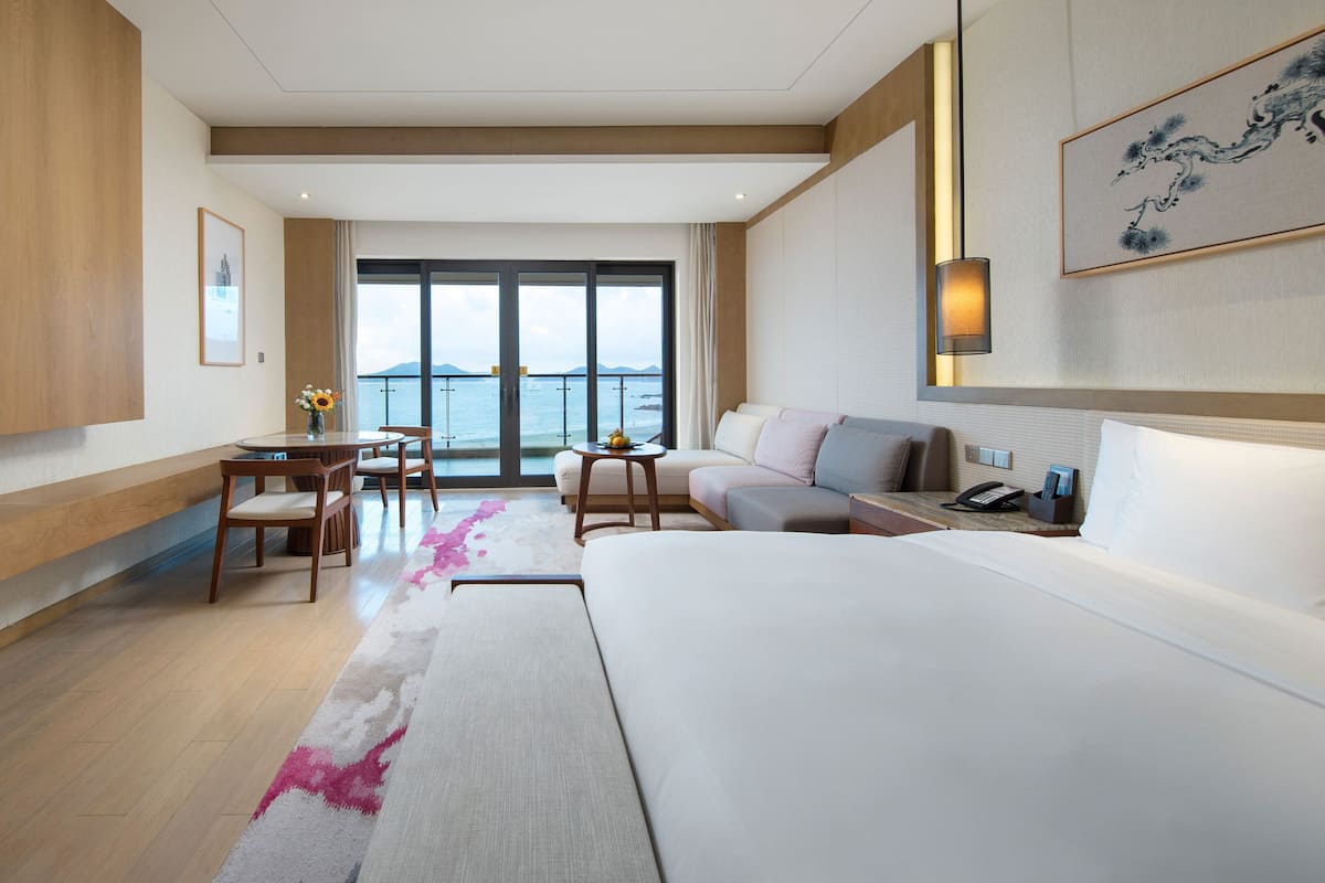 Une chambre d’hôtel moderne, dotée d’un grand lit, d’un bureau avec une chaise, d’un canapé et d’un téléviseur fixé au mur.