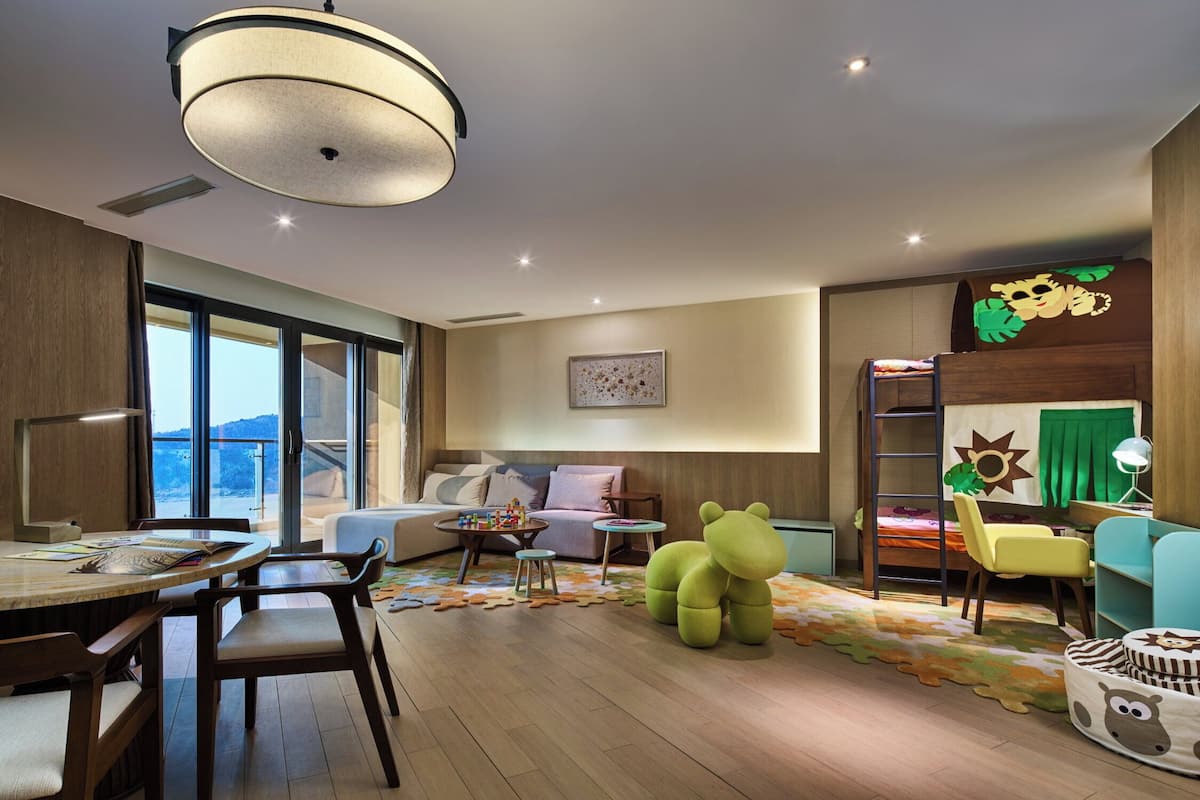 Un salon moderne comprenant un coin repas, un canapé, un espace de jeux avec un fauteuil en forme d’ours et une échelle menant à un lit en mezzanine.