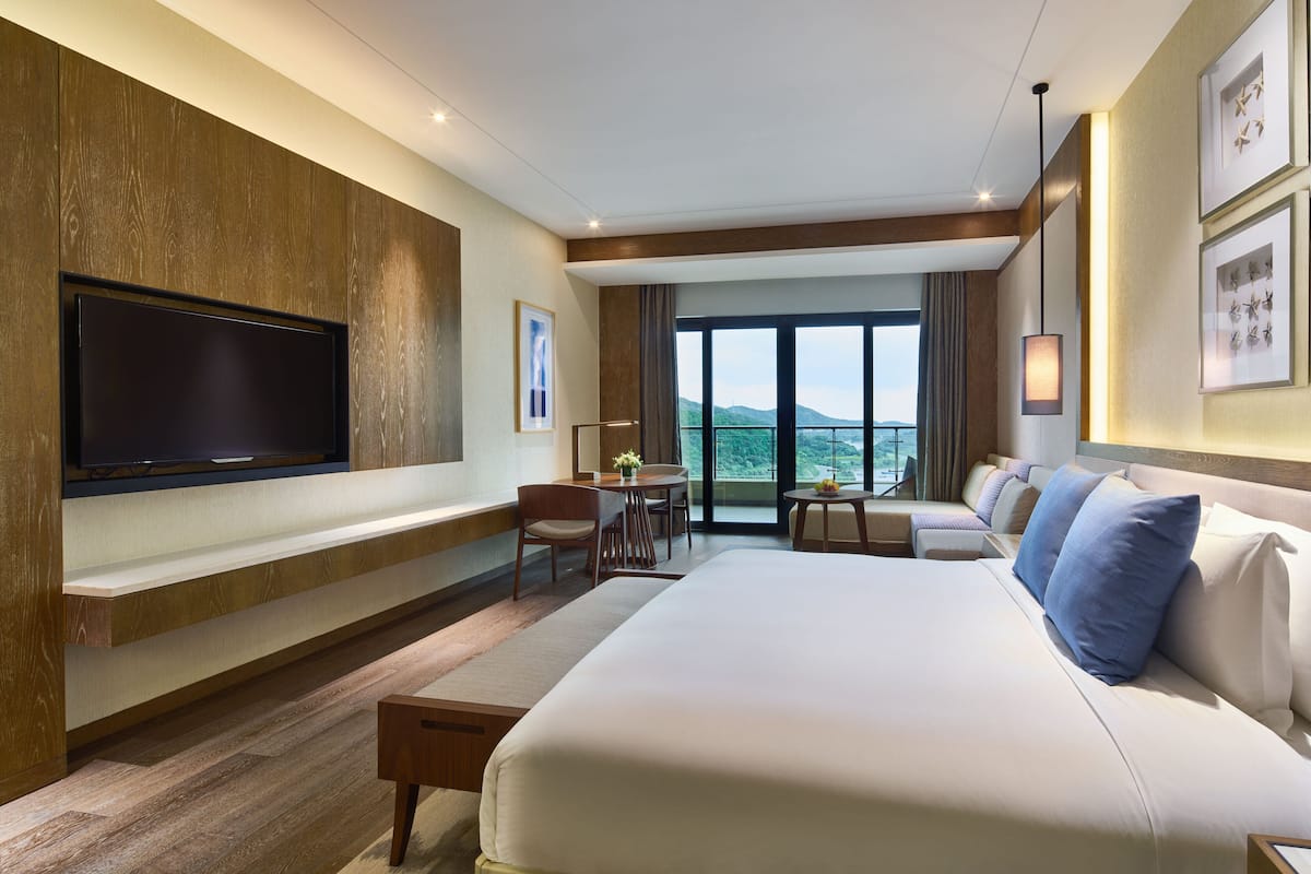 Une chambre d’hôtel dotée d’un grand lit, d’un téléviseur à écran plat fixé au mur, d’un balcon avec vue et d’un coin repas comprenant une table et des chaises.