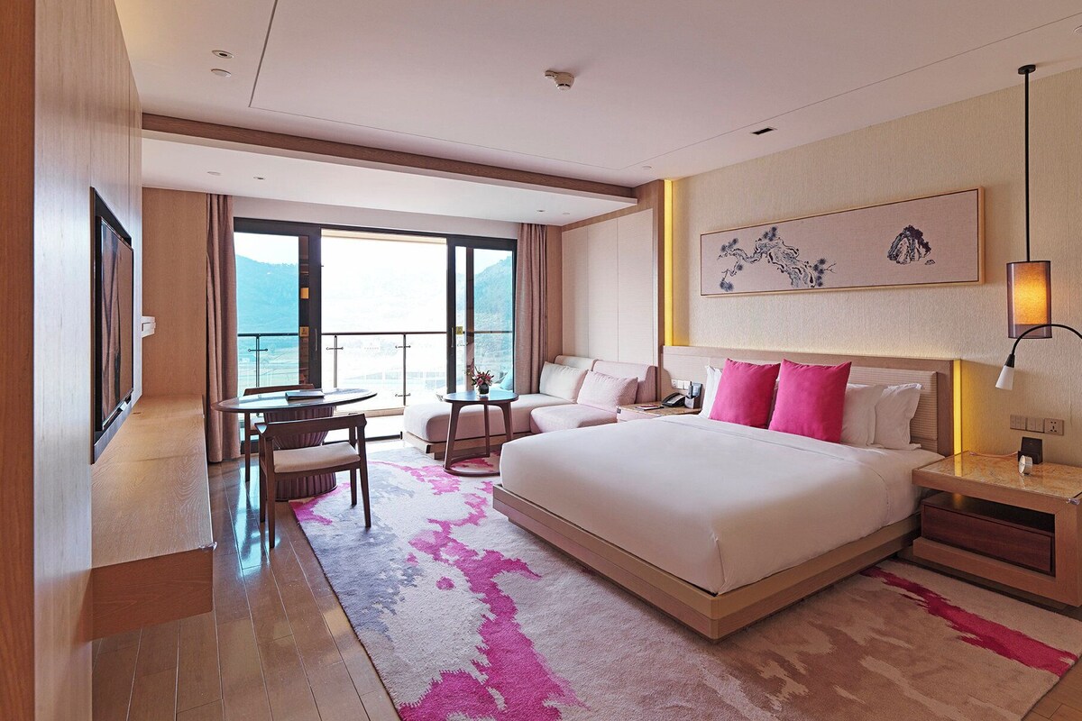 Une chambre d’hôtel avec un grand lit, un bureau, une chaise, un canapé et une vue sur la mer.