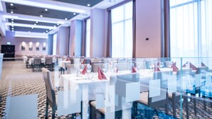 Un vaste espace de restauration d’hôtel, avec des tables dressées pour les clients, de grandes fenêtres et un design moderne au plafond.