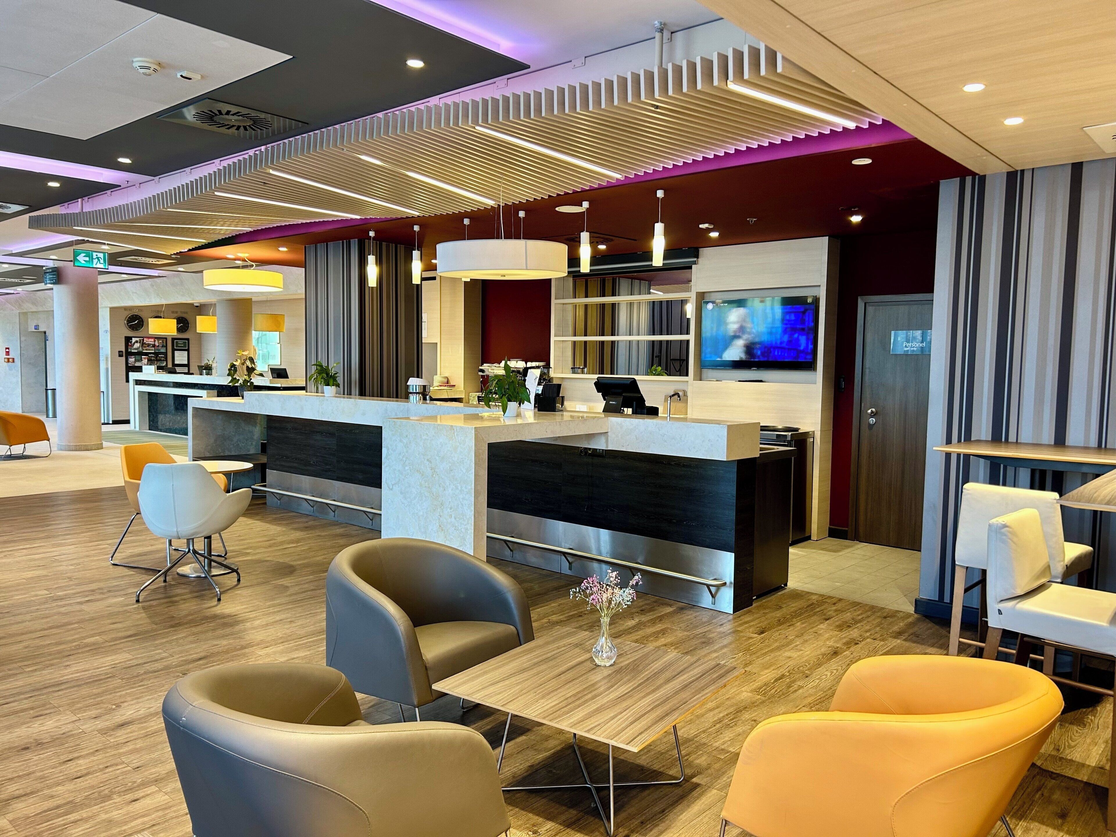 Un moderno hall de hotel con mostrador de recepción, zona de estar y pantalla de televisión.