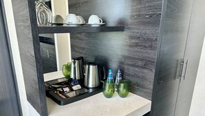 Une cuisine moderne avec un plan de travail, une machine à café, des verres verts et une étagère où sont posées des tasses et une bouilloire.