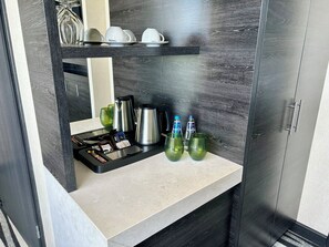 A modern kitchen with a countertop, coffee maker, green glass cups, and a shelf with cups and a kettle. - Holiday Inn Dabrowa Gornicza by IHG (Dabrowa Gornicza)