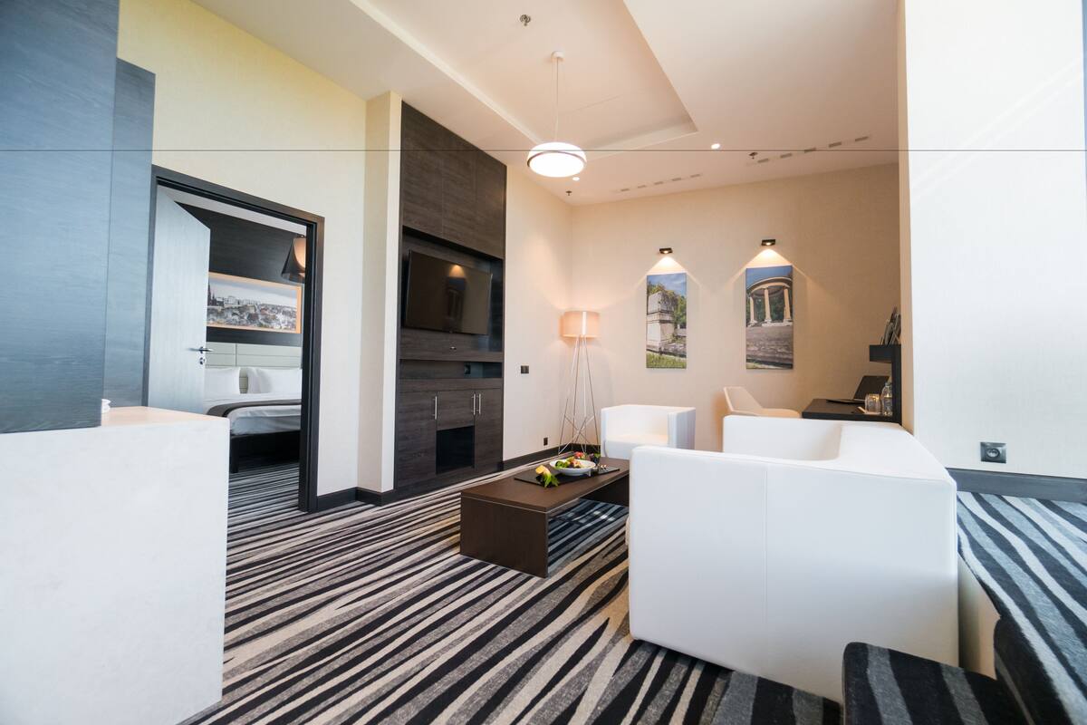 A modern hotel room with a sofa, a coffee table, a TV, and a bed.