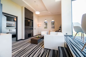 A modern hotel room with a large bed, a dining area with a table and chairs, a fireplace, and a view of the outdoors. - Holiday Inn Dabrowa Gornicza by IHG (Dabrowa Gornicza)
