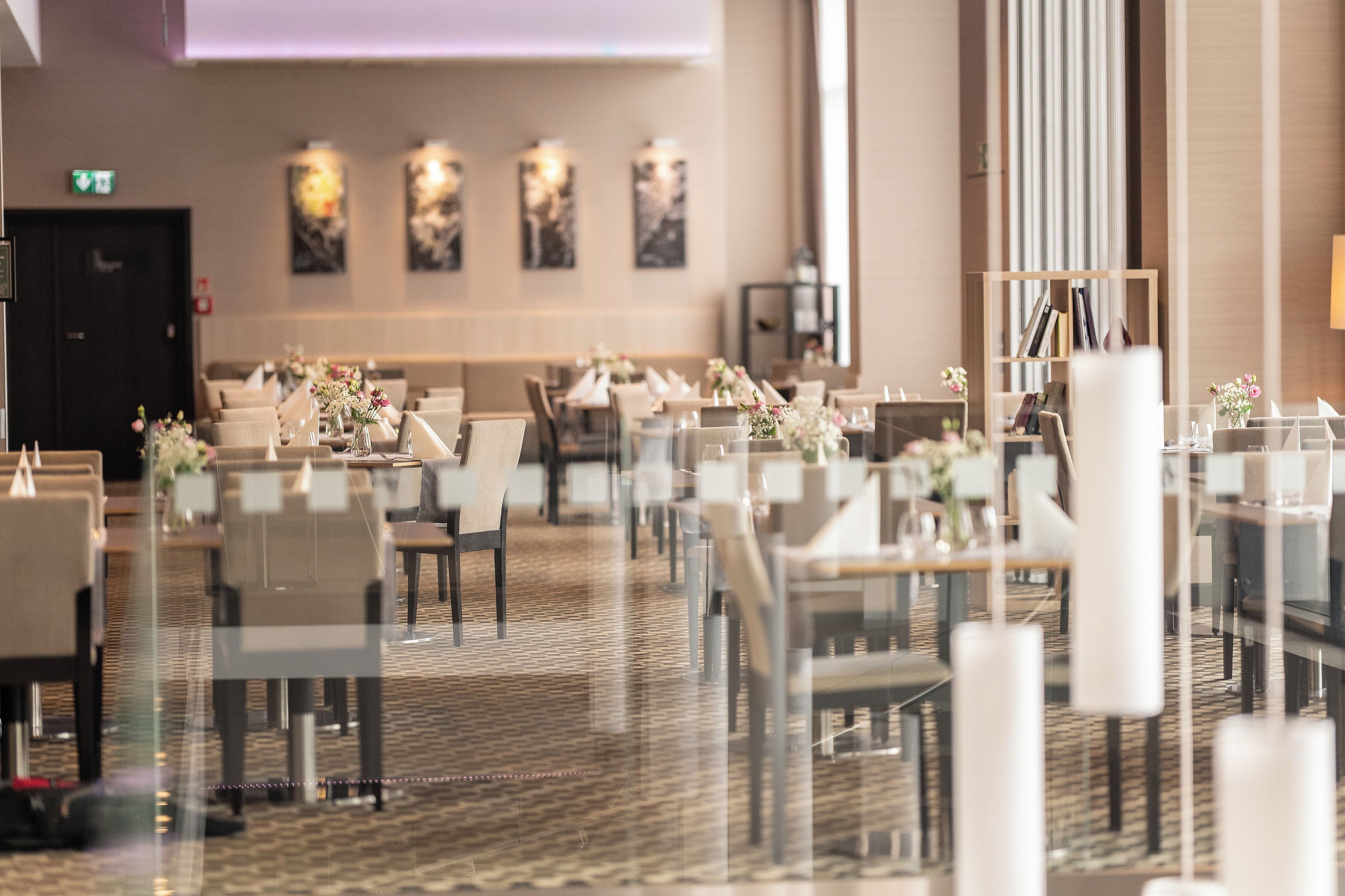 A hotel dining area with tables set for guests, chairs, and a patterned carpet.