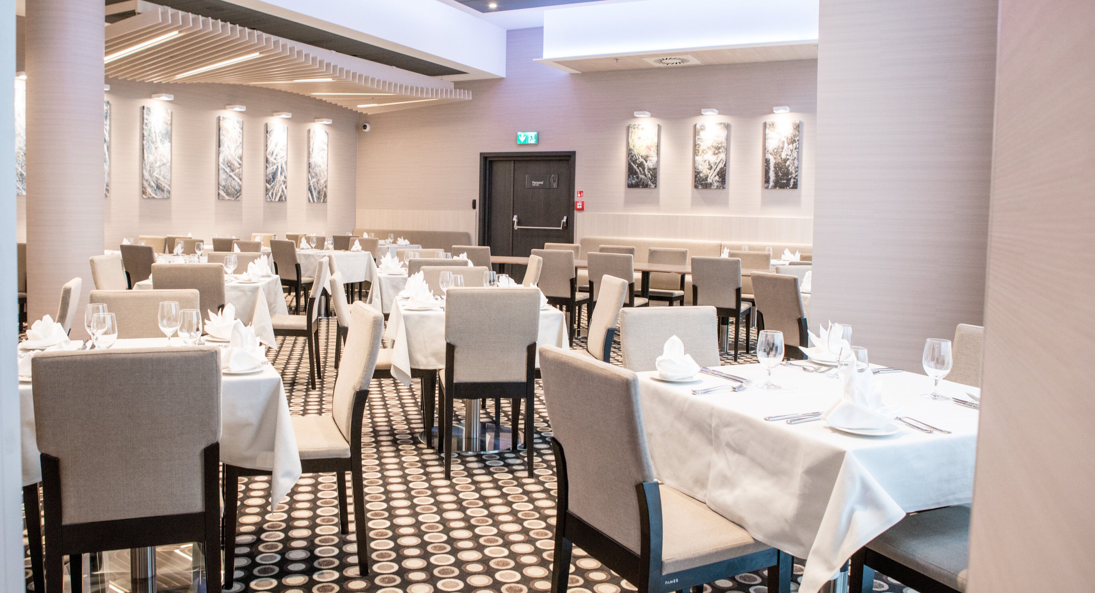 Ein Hotel-Speisesaal mit mehreren für Gäste gedeckten Tischen, mit einem gemusterten Boden und moderner Einrichtung.
