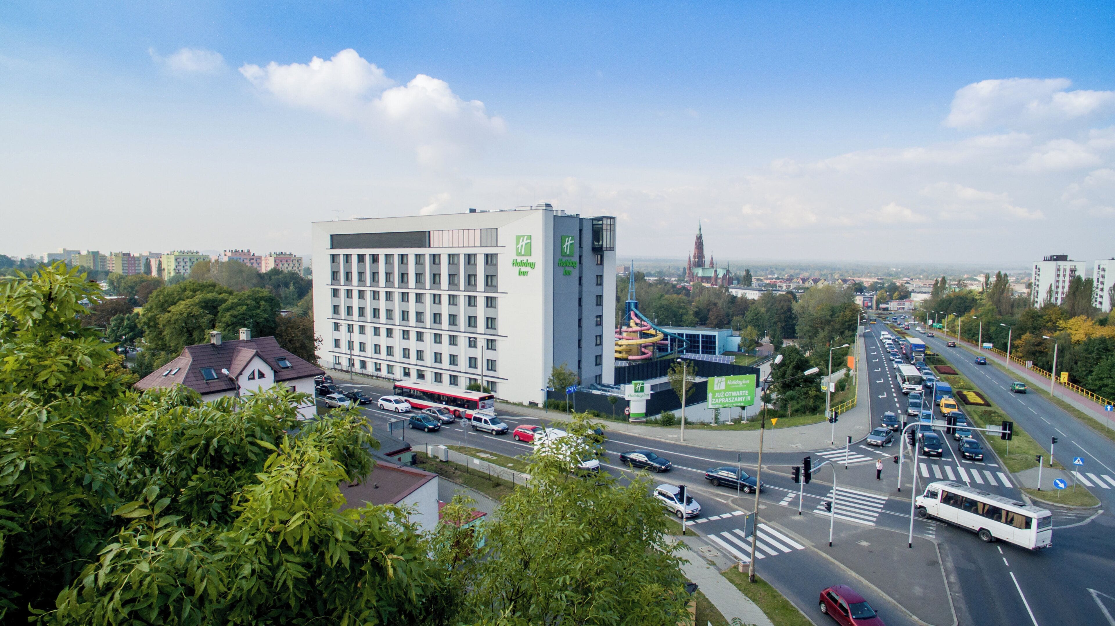 Hotel Holiday Inn amb un disseny modern, situat a prop d'un encreuament amb trànsit i una vista del skyline urbà al fons.