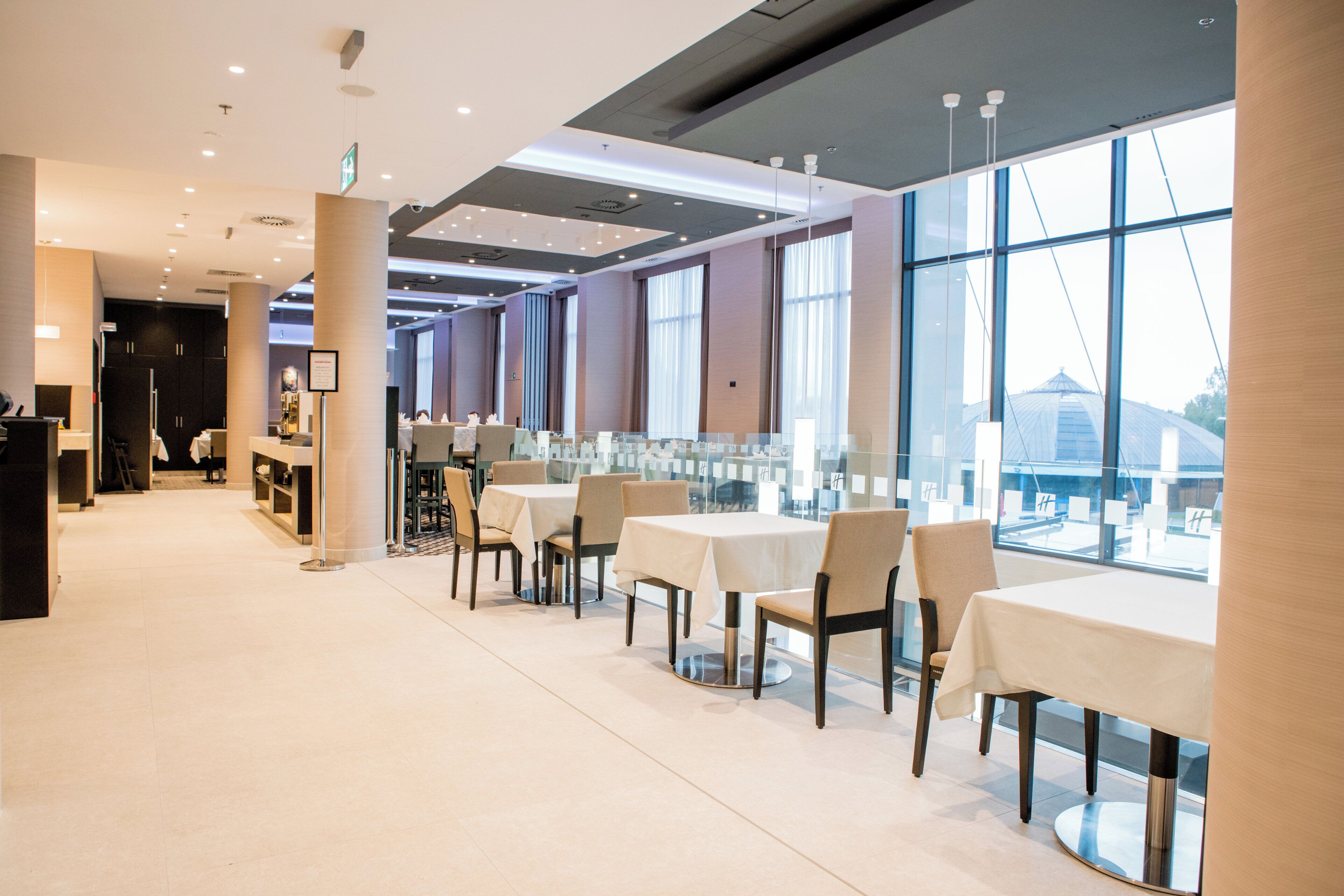 A modern restaurant with high ceilings, large windows, and a clean, minimalist interior.