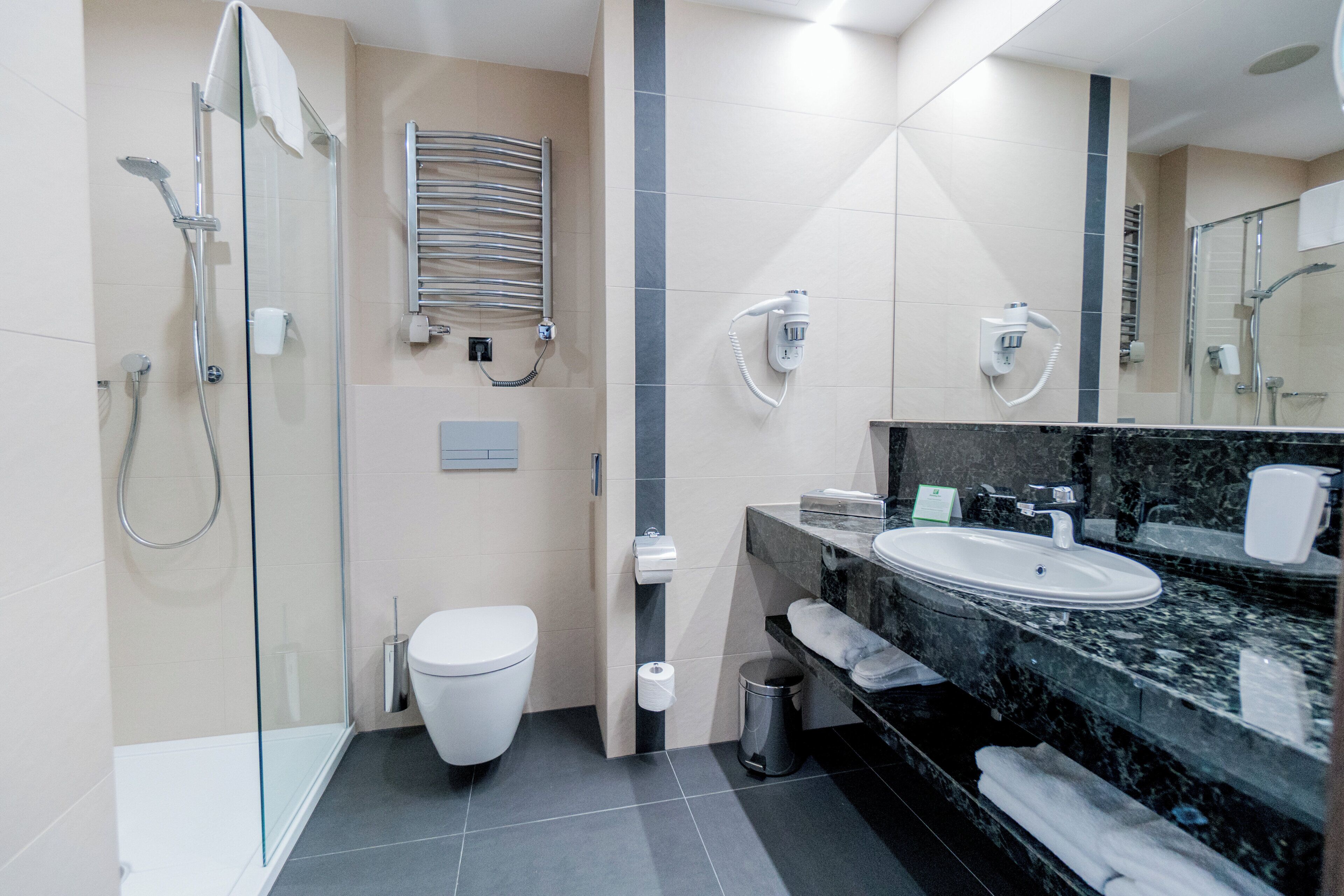 Un baño moderno con cabina de ducha de vidrio, inodoro, lavabo con encimera de mármol y toallero.
