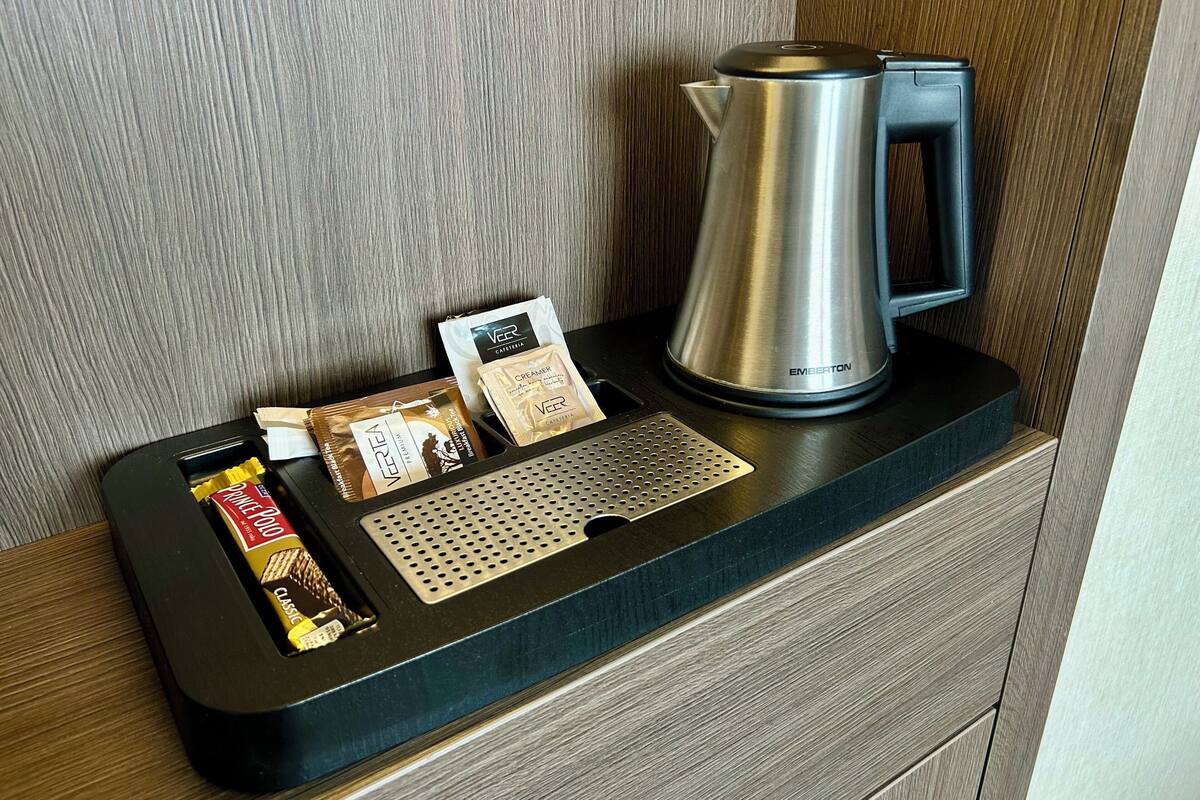 A coffee maker, a coffee pod, a creamer packet, and a chocolate bar on a wooden counter.