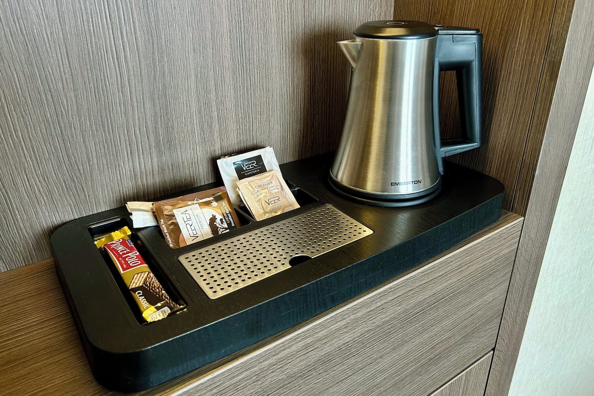 A coffee maker, a coffee pod, a creamer packet, and a chocolate bar on a wooden counter.