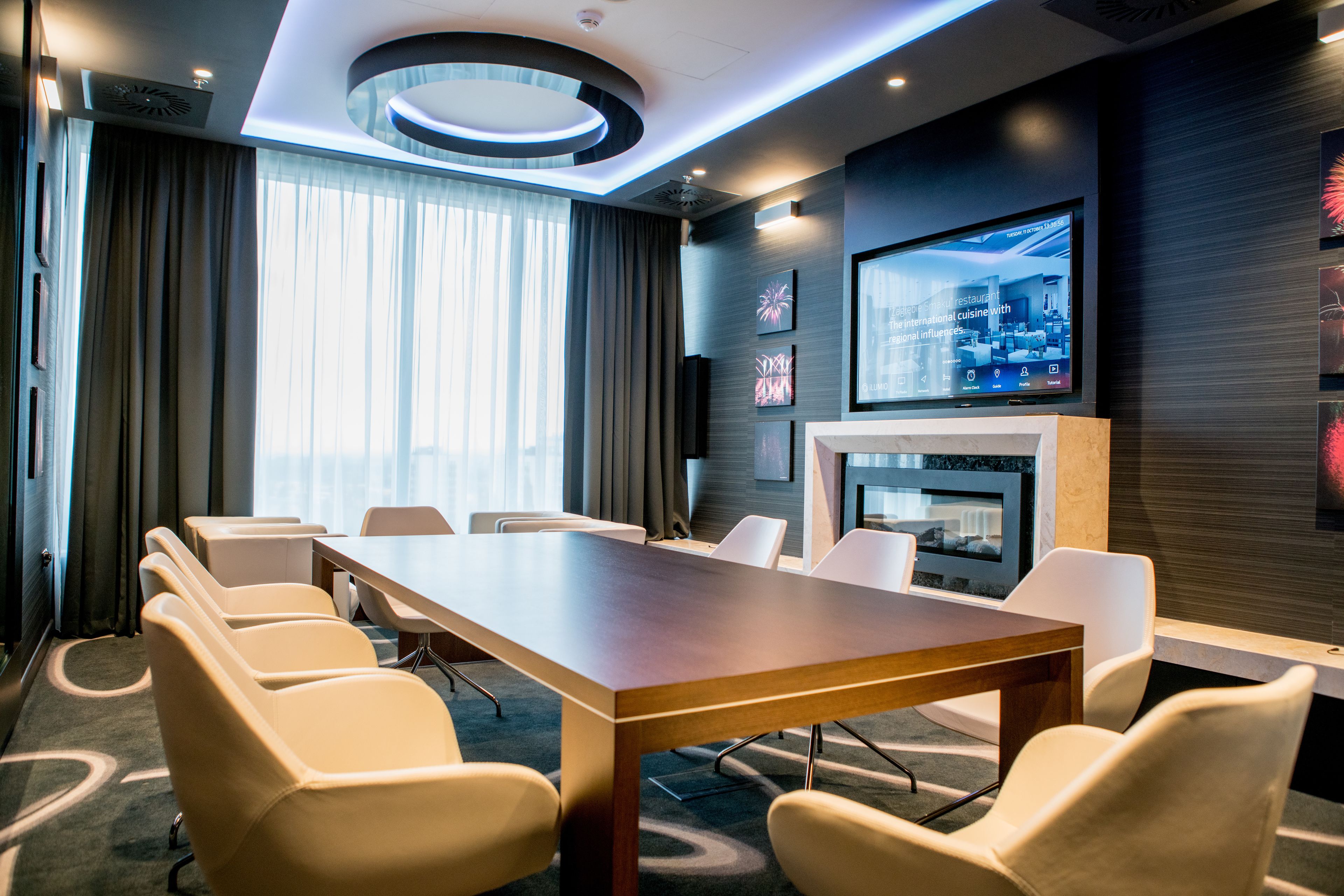 A modern conference room with a long table, six chairs, a flat-screen TV, and a fireplace.