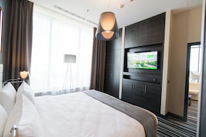 A hotel room with a large bed, a flat-screen TV mounted on the wall, a desk with a lamp, and a view of the outdoors through the window. - Holiday Inn Dabrowa Gornicza by IHG (Dabrowa Gornicza)