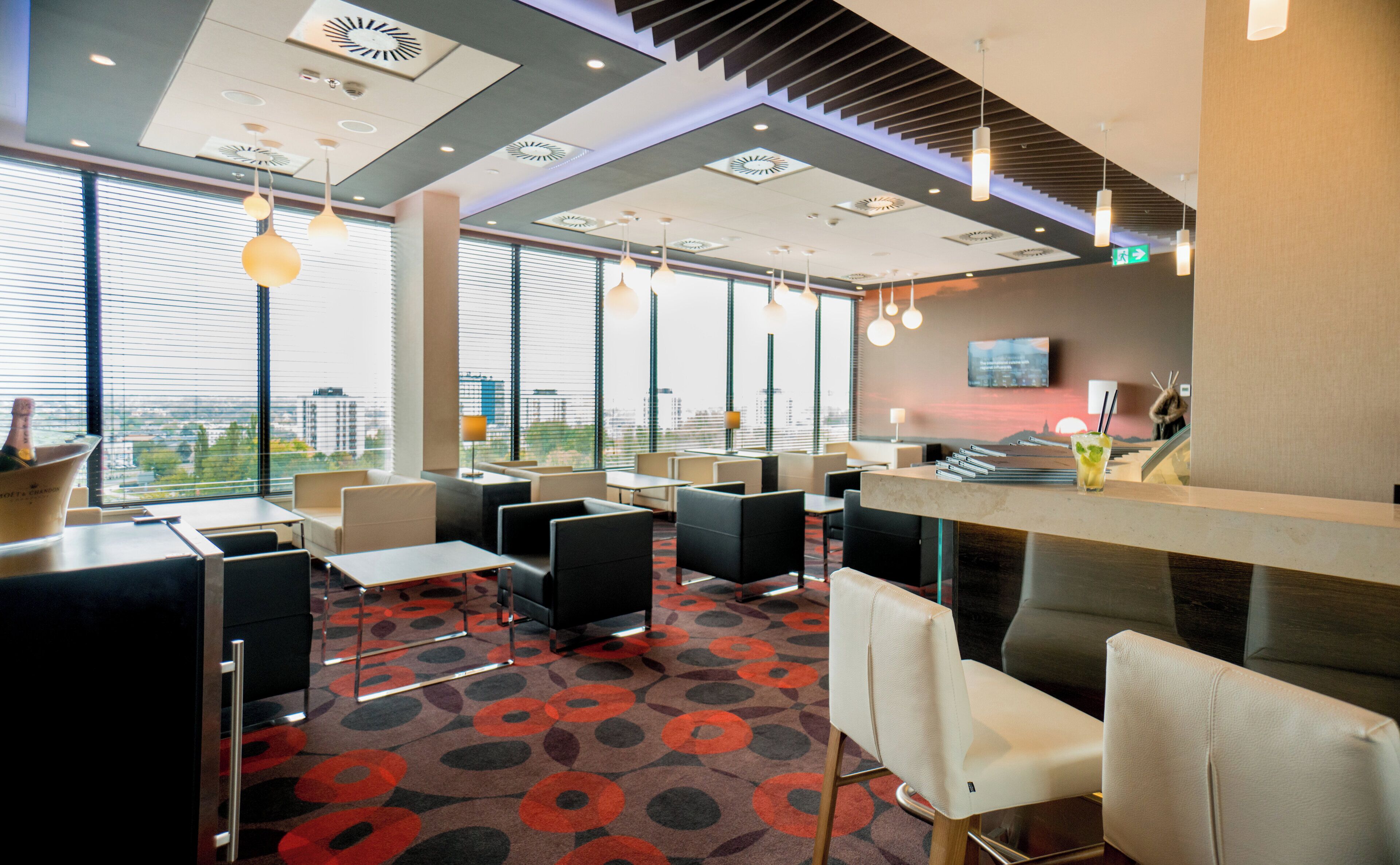 A modern hotel lobby with seating areas, a reception desk, and large windows offering a city view.