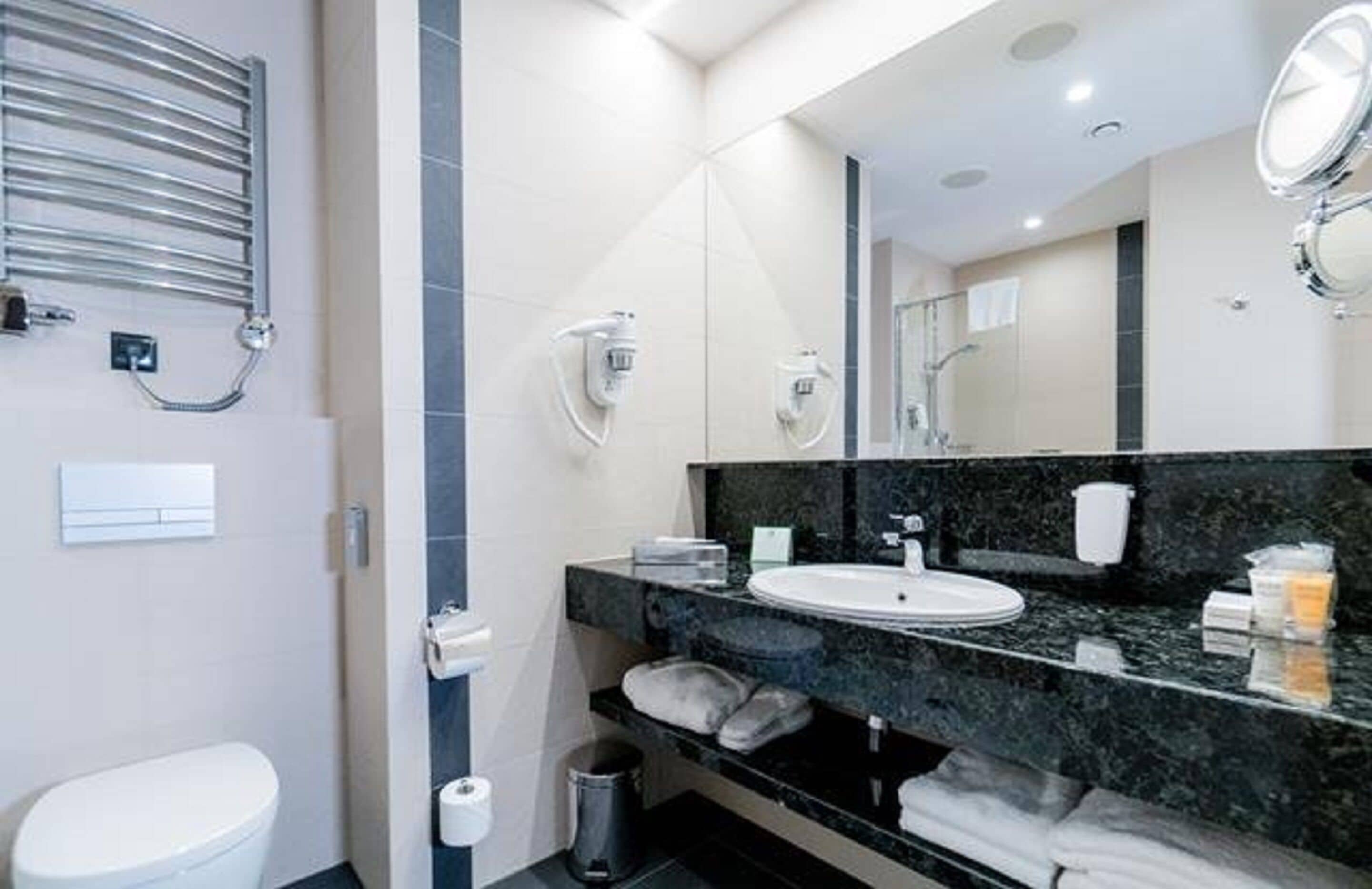 A modern bathroom with a white toilet, a black marble sink, a large mirror, and a towel rack.