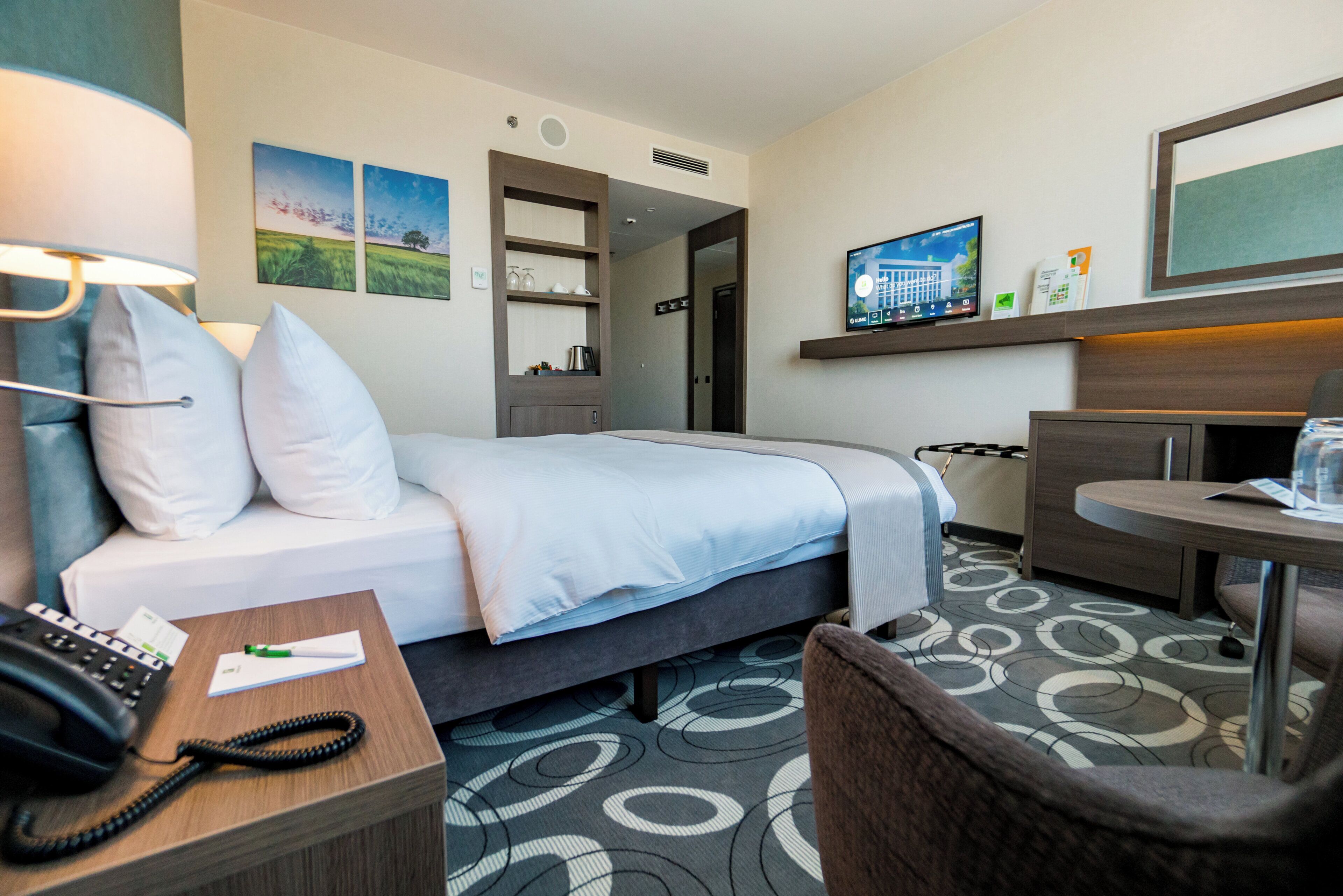 A hotel room with a bed, a desk with a telephone, a chair, a television, and a small table.