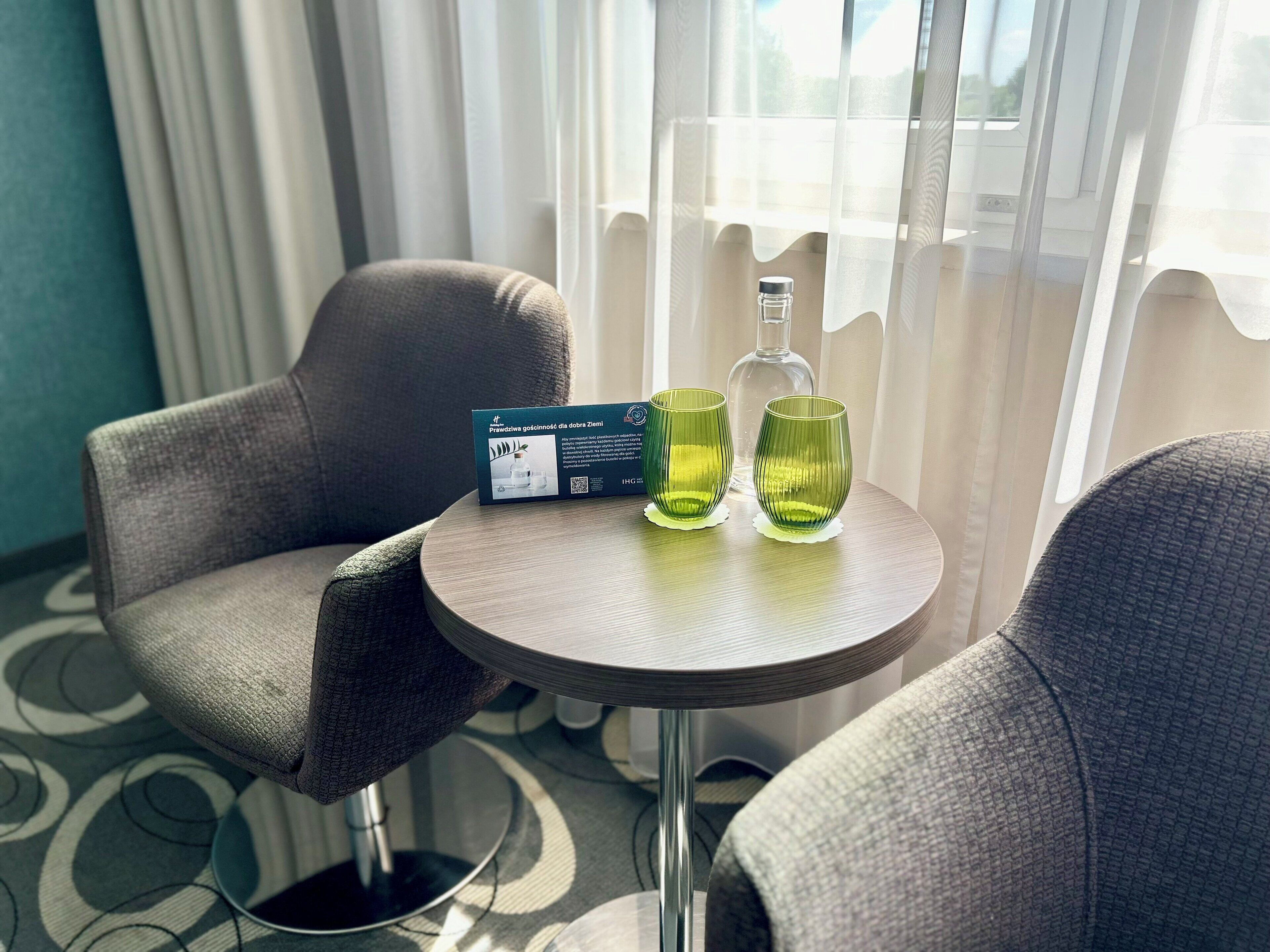 Una habitació d'hotel amb una taula rodona, dues cadires, una ampolla i una caixa de productes d'higiene.