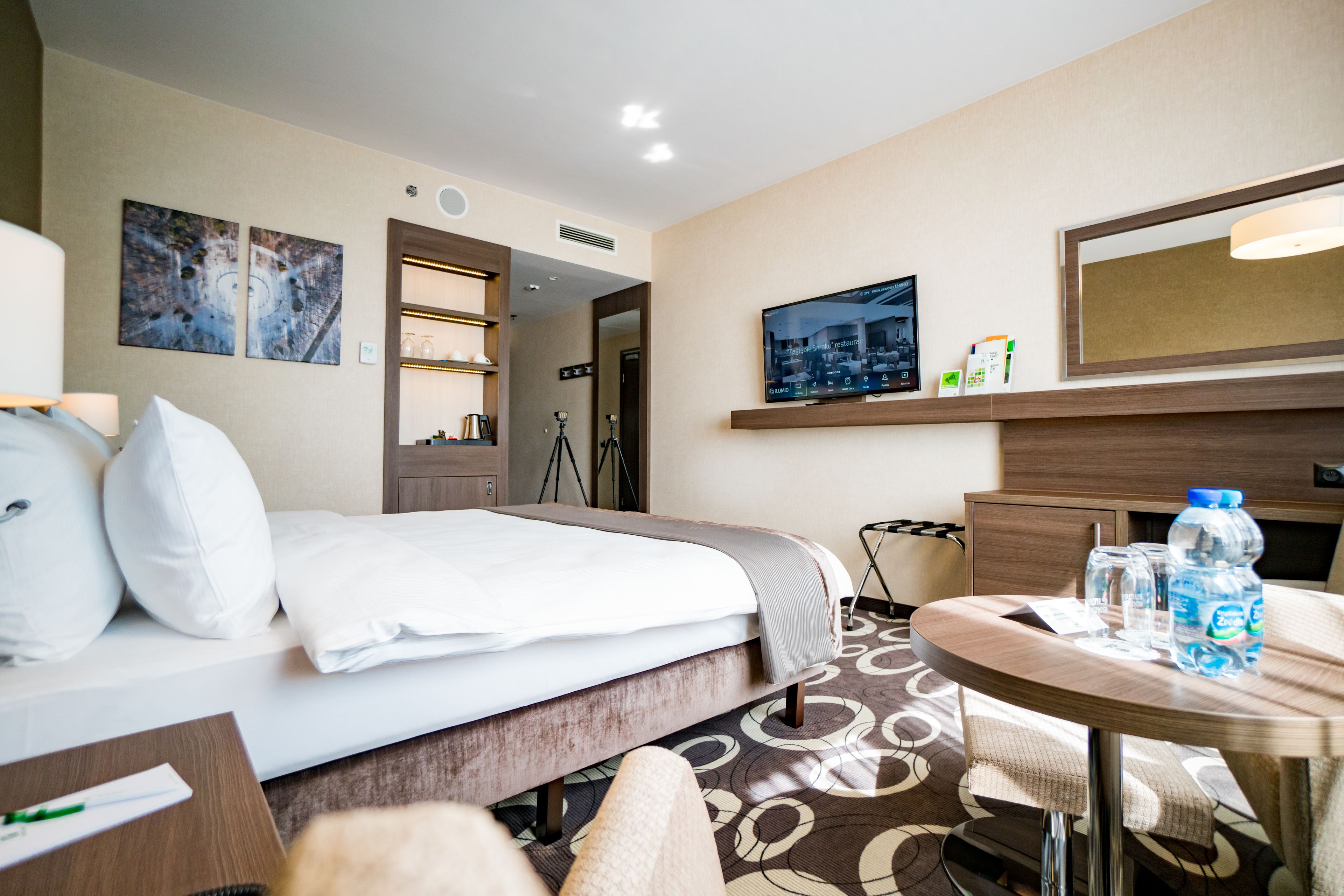 A hotel room with a bed, a round table with chairs, a TV, and a mirror.