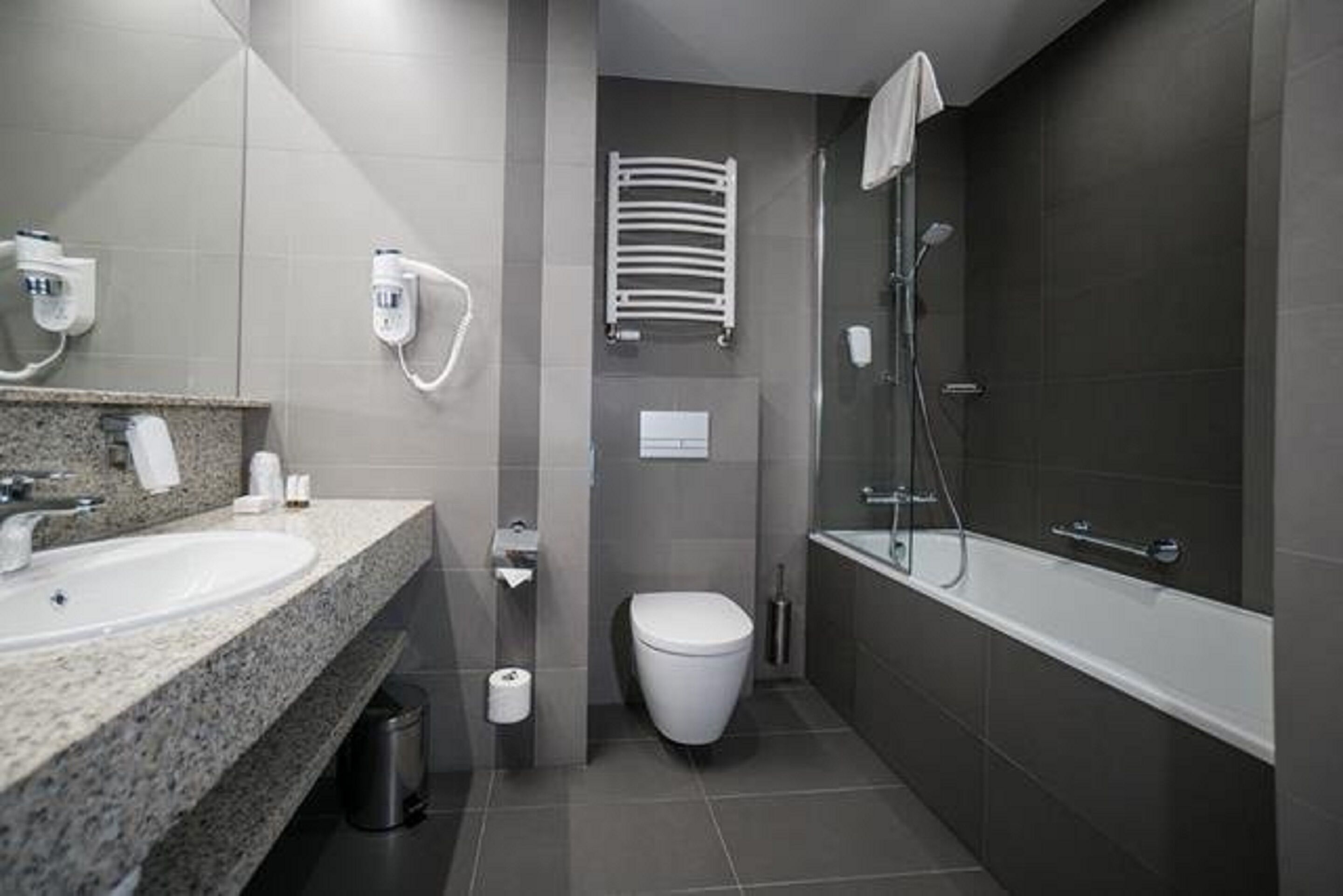 Un bany modern amb taulell de granat, un vàter blanc, una cabina de dutxa de vidre i un suport per a tovalloles.