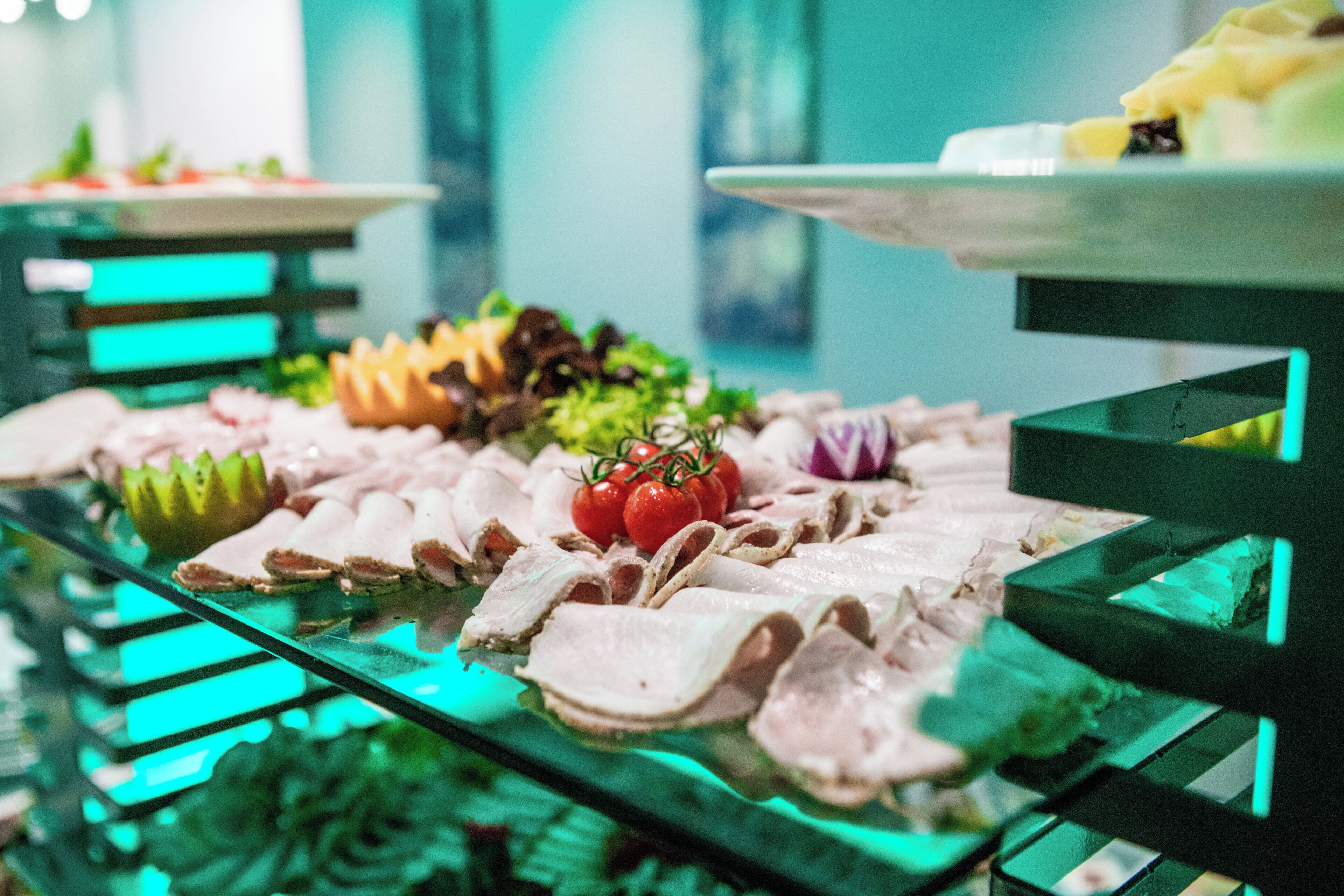 A buffet with various food items including sliced meats, vegetables, and a fruit bowl.