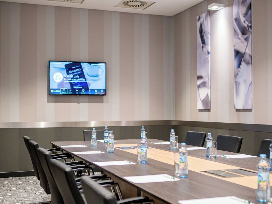 A conference room with a long table, chairs, water bottles, and a screen displaying a QR code pairing app.
