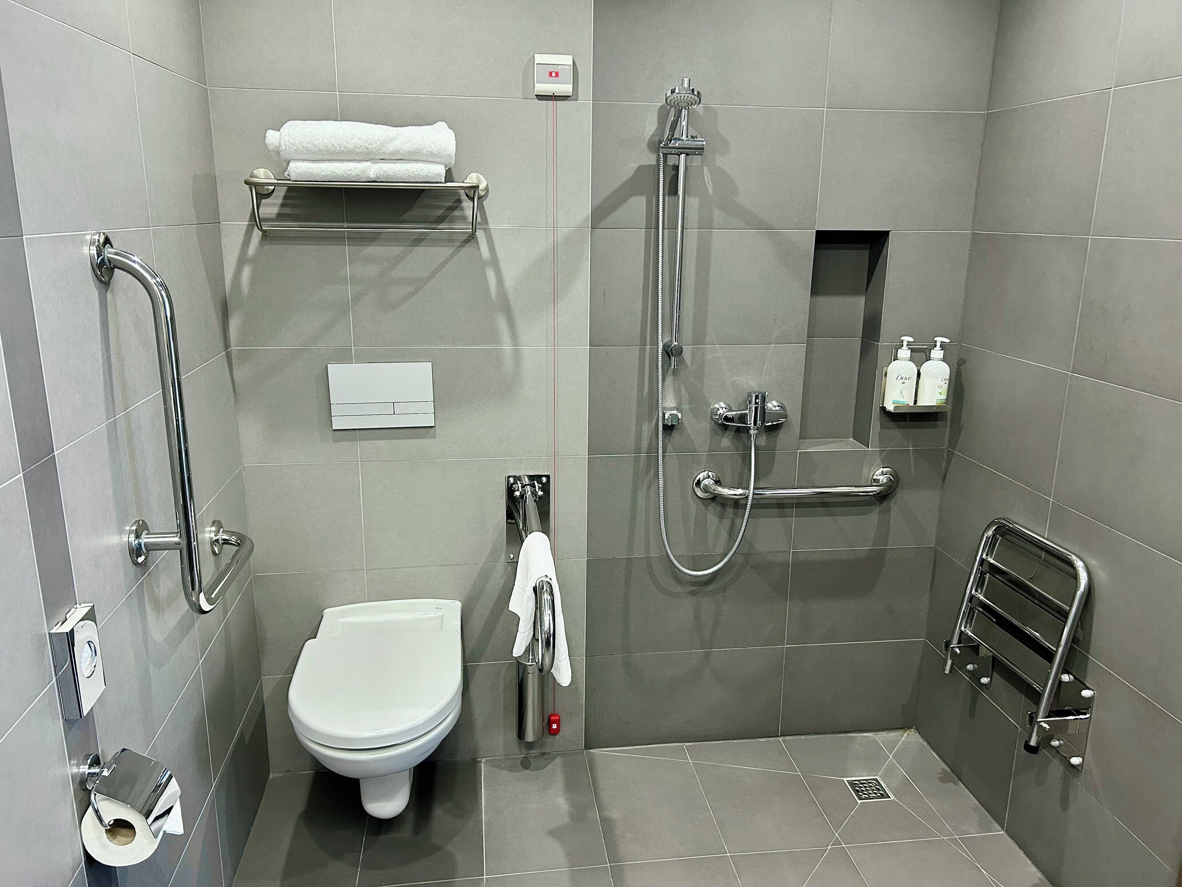 Un baño moderno con inodoro, ducha, toallero y dispensador de jabón.