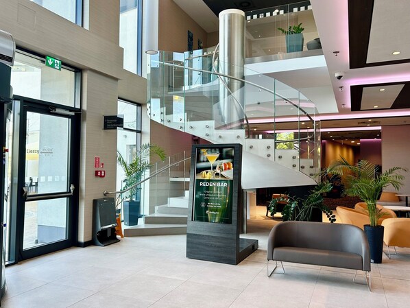 A modern hotel lobby with a glass staircase, a reception desk, and a sign for the Red Bar. - Holiday Inn Dabrowa Gornicza by IHG (Dabrowa Gornicza)