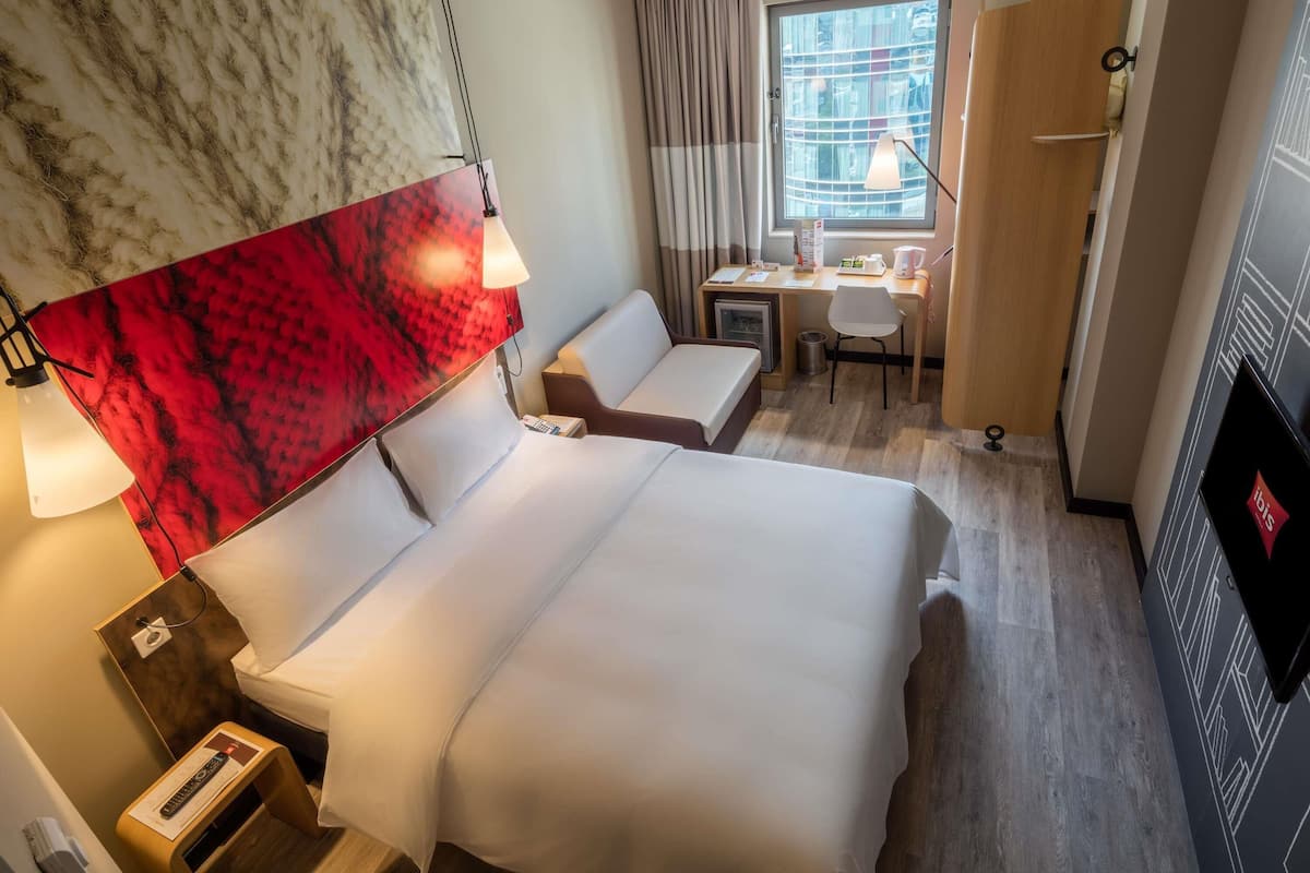 A hotel room with two beds, a desk, a chair, a TV, and a window with curtains.