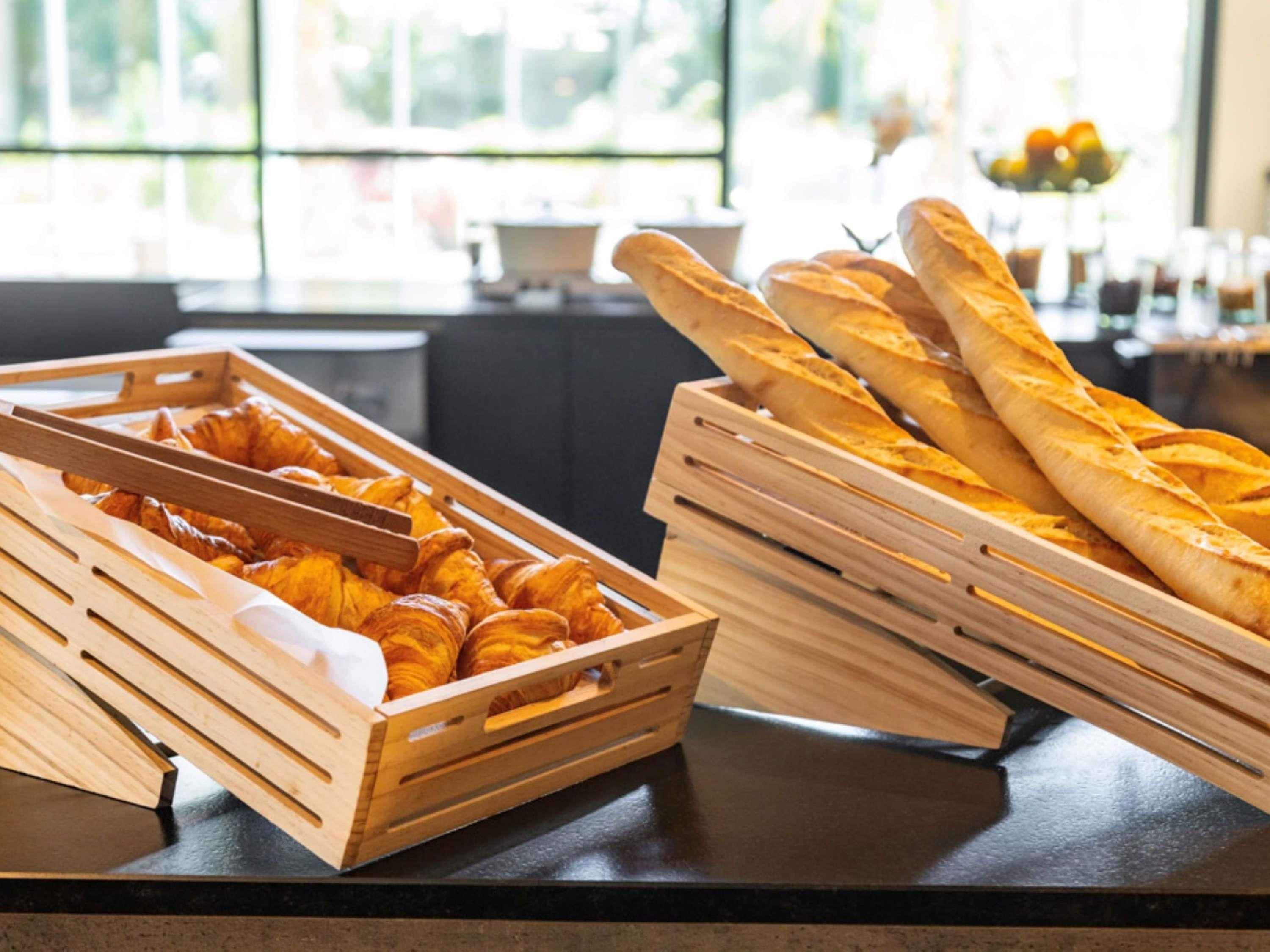 A breakfast buffet with croissants and baguettes in wooden crates.