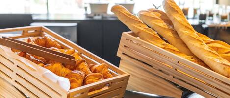 A breakfast buffet with croissants and baguettes in wooden crates.