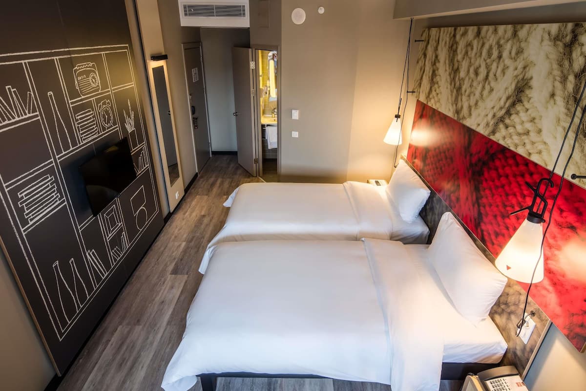 A hotel room with two beds, a large wall mural, a desk with a lamp, and a phone on the side table.