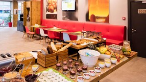 A restaurant with red seating, a buffet with various food items, and a television screen on the wall. - ibis Istanbul West (Istanbul)