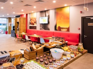 A restaurant with red seating, a buffet with various food items, and a television screen on the wall. - ibis Istanbul West (Istanbul)