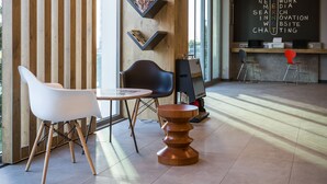 A modern interior with a reception desk, seating area, and large windows allowing natural light. - ibis Istanbul West (Istanbul)