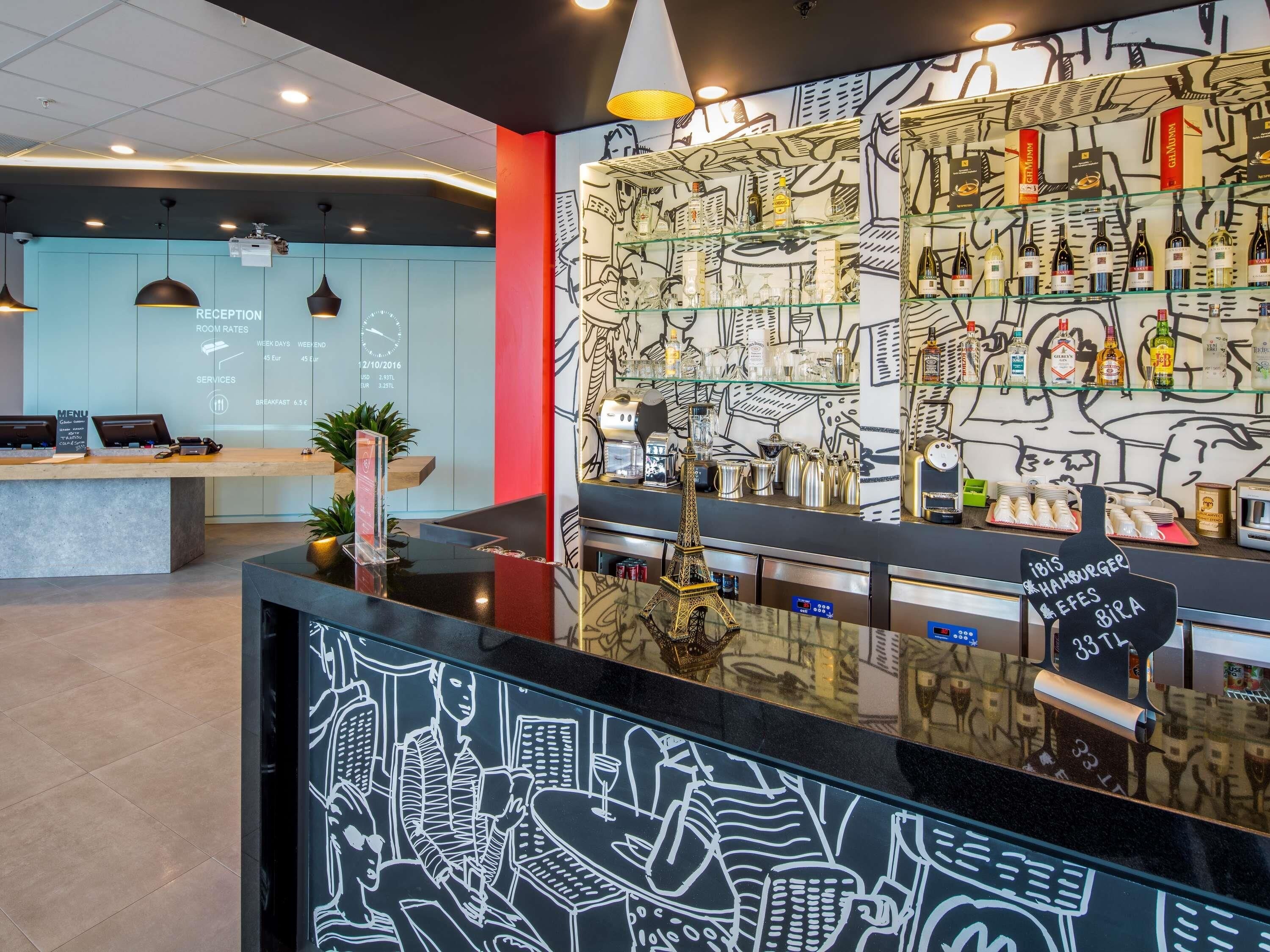A hotel reception area with a modern design, including a reception desk, a menu board, and a wall with a cityscape mural.