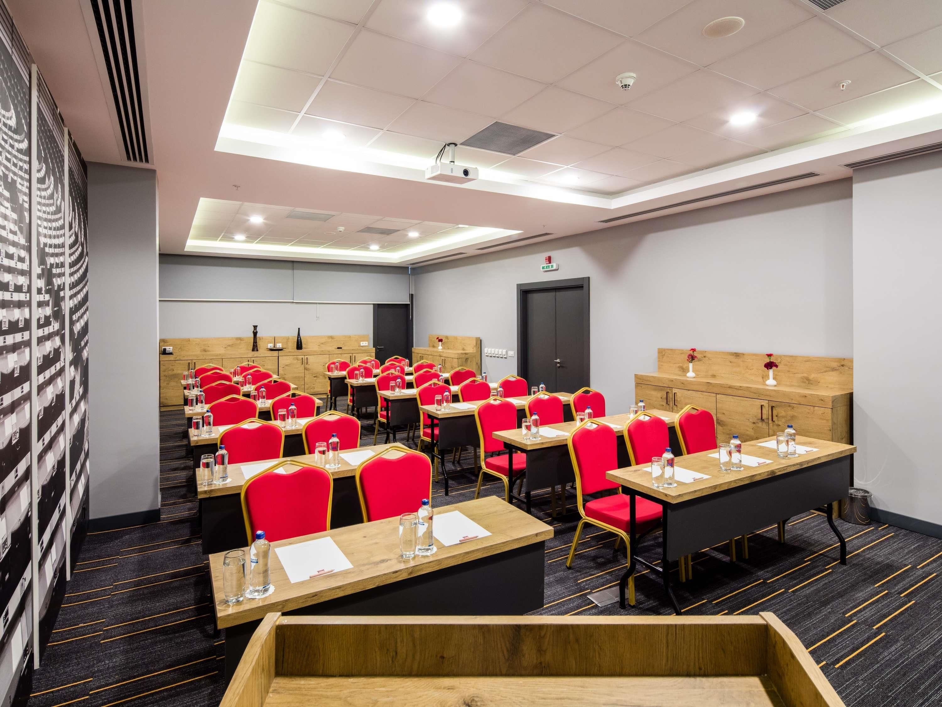 A conference room with rows of tables and chairs, equipped with water bottles and papers.