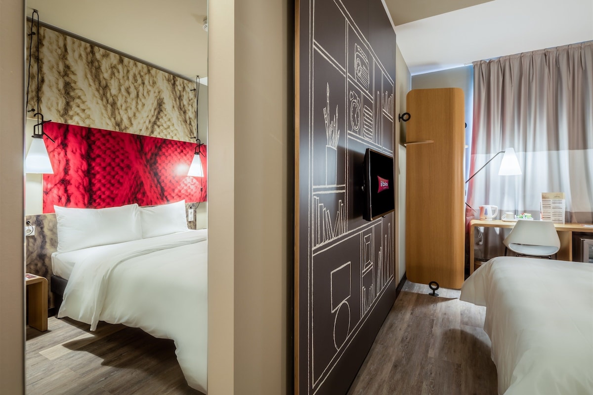 A hotel room with a bed, a desk, a TV, and a mirror.