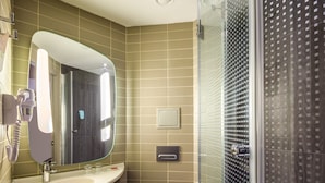 A modern bathroom with a large mirror, a sink, a toilet, and a glass-enclosed shower. - ibis Istanbul West (Istanbul)