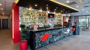 A modern reception area with a black and white mural, red accents, and a seating area with red chairs. - ibis Istanbul West (Istanbul)